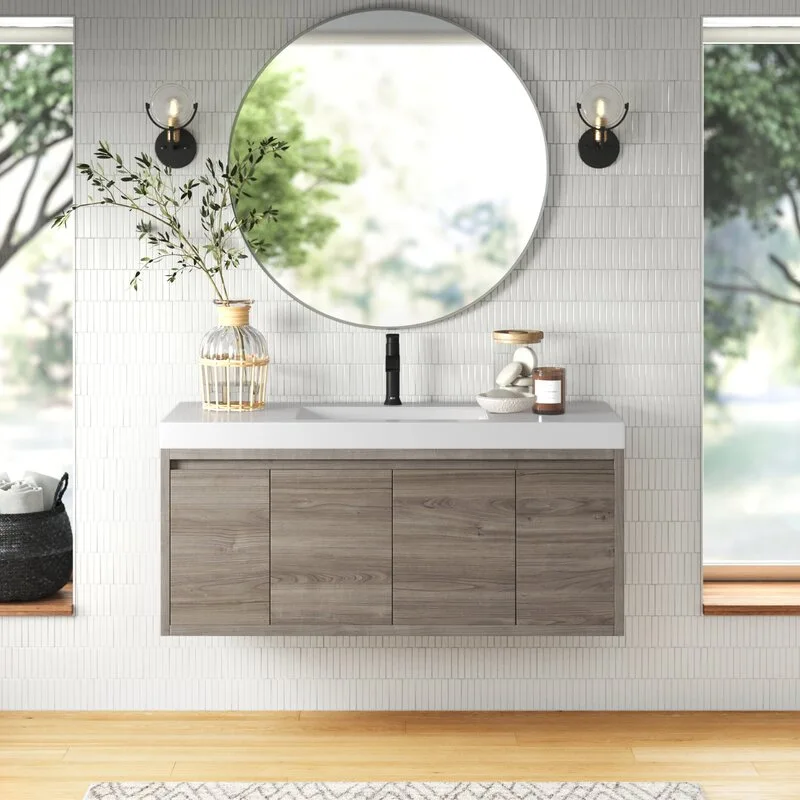 A floating wood vanity with a white countertop sits against a white vertically tiled wall beneath a large round mirror flanked by black sconces.