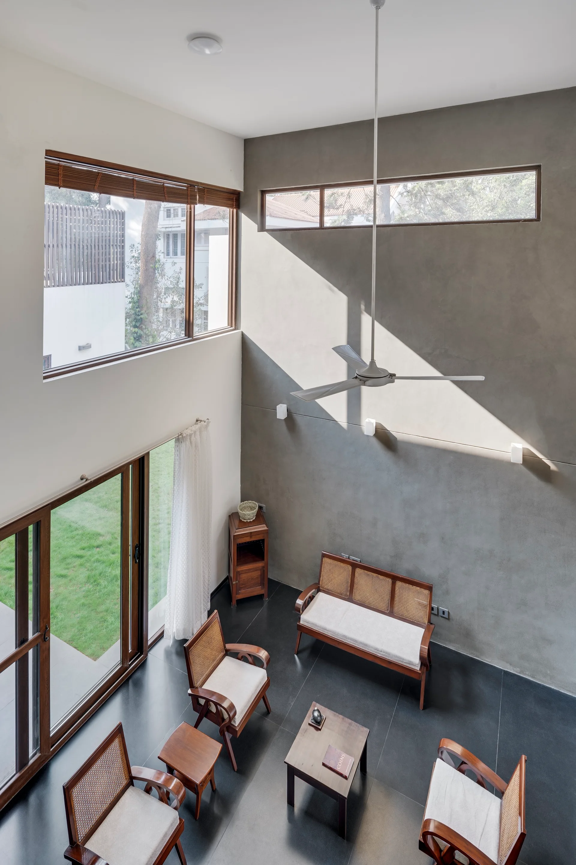High-angle view of a modern living room featuring a concrete accent wall, dark floor tiles, and mid-century wooden armchairs with cane backs.
