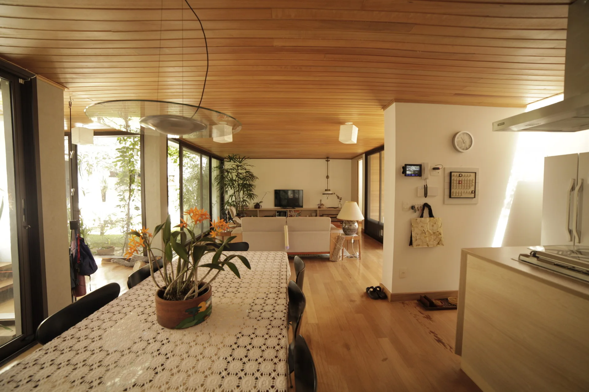 An open-concept living and dining area features a wood-plank ceiling, hardwood floors, a long dining table, and large sliding glass doors.