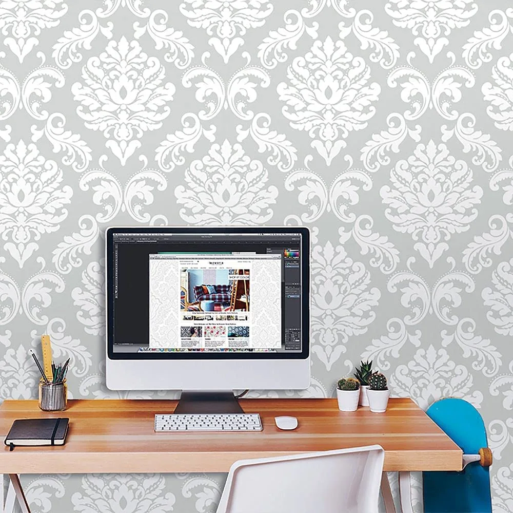 A wooden desk with a computer monitor and small potted plants sits against a wall covered in gray and white damask wallpaper.