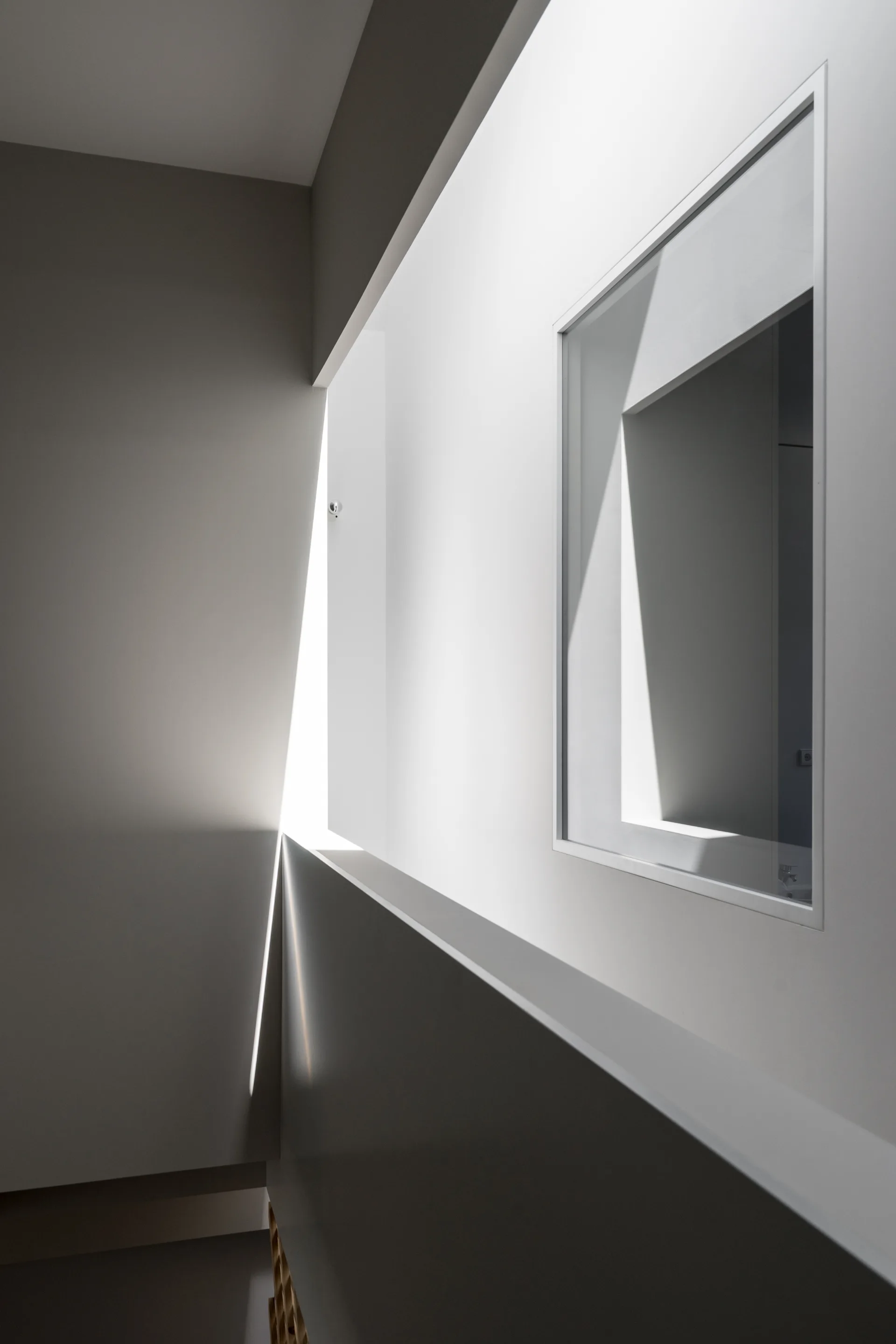 A deep recessed square window in a minimalist white wall with sharp geometric shadows cast by natural light.