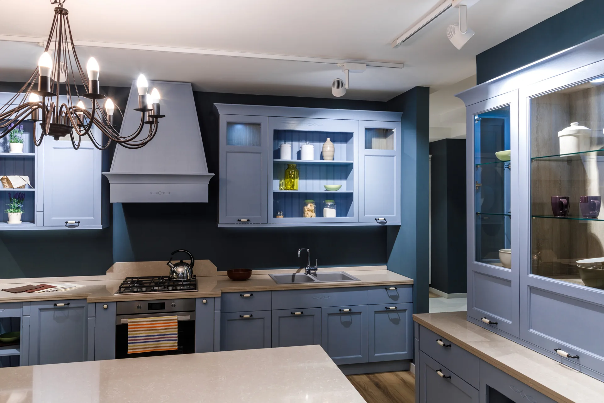Blue shaker-style kitchen cabinetry with beige stone countertops against a dark gray accent wall.