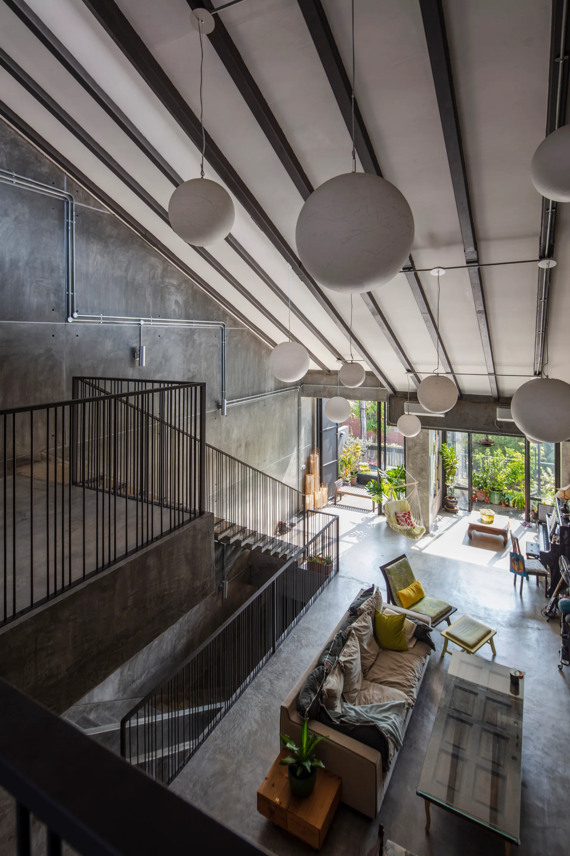 High-angle view of an industrial living room featuring concrete walls, a vaulted ceiling with dark beams, and globe pendant lights.