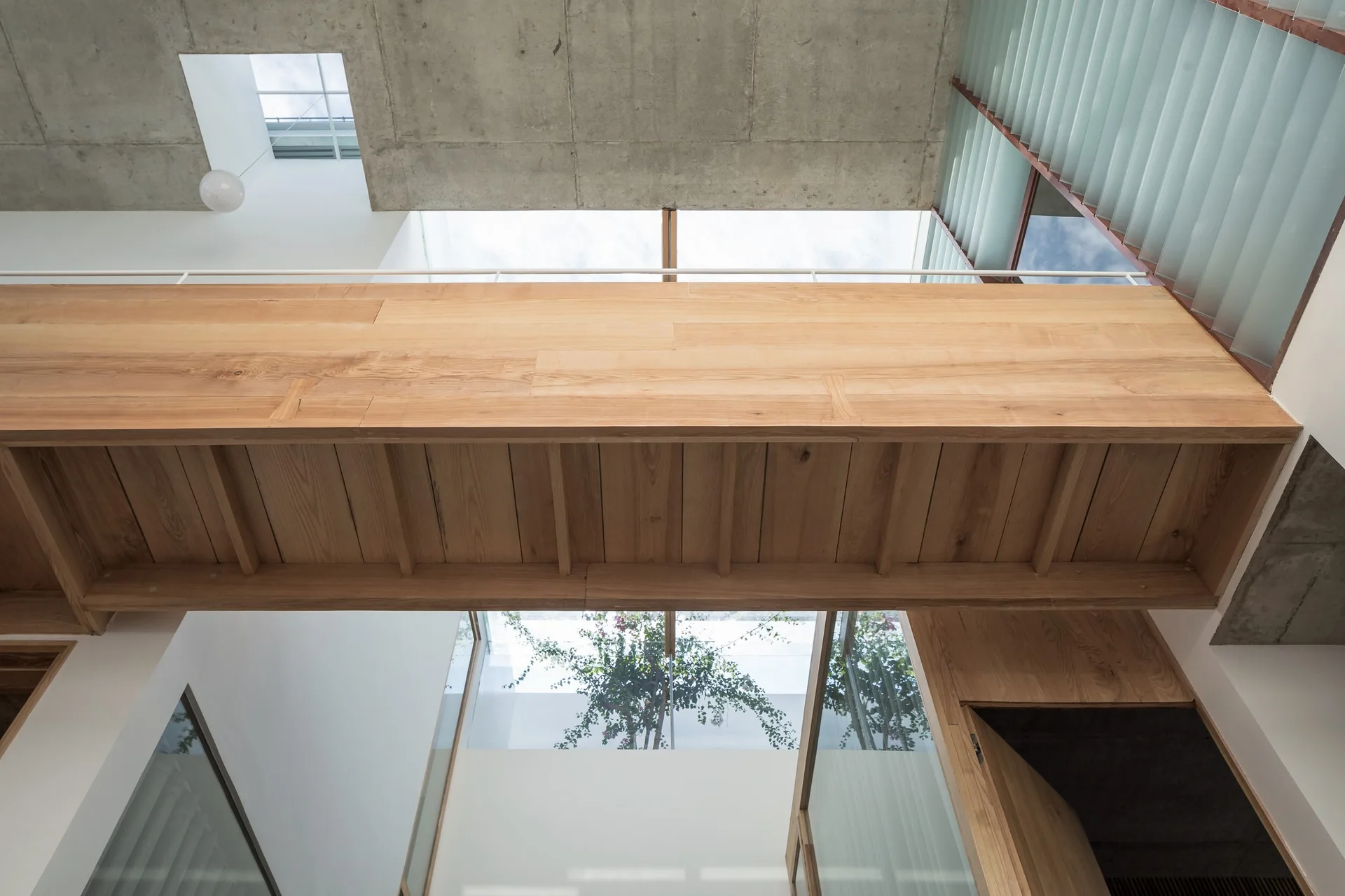 An upward view of a modern atrium showing an elevated light wood bridge beneath an exposed concrete ceiling with skylights.