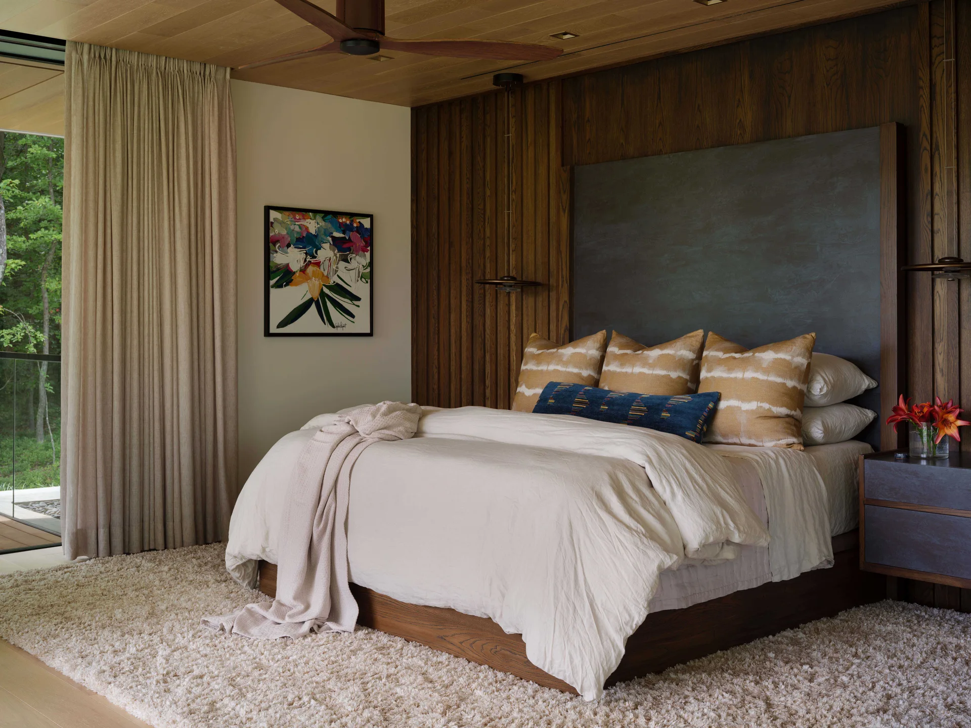 A contemporary bedroom featuring a bed with white linen bedding against a dark vertical wood slat wall, topped with a wood plank ceiling.