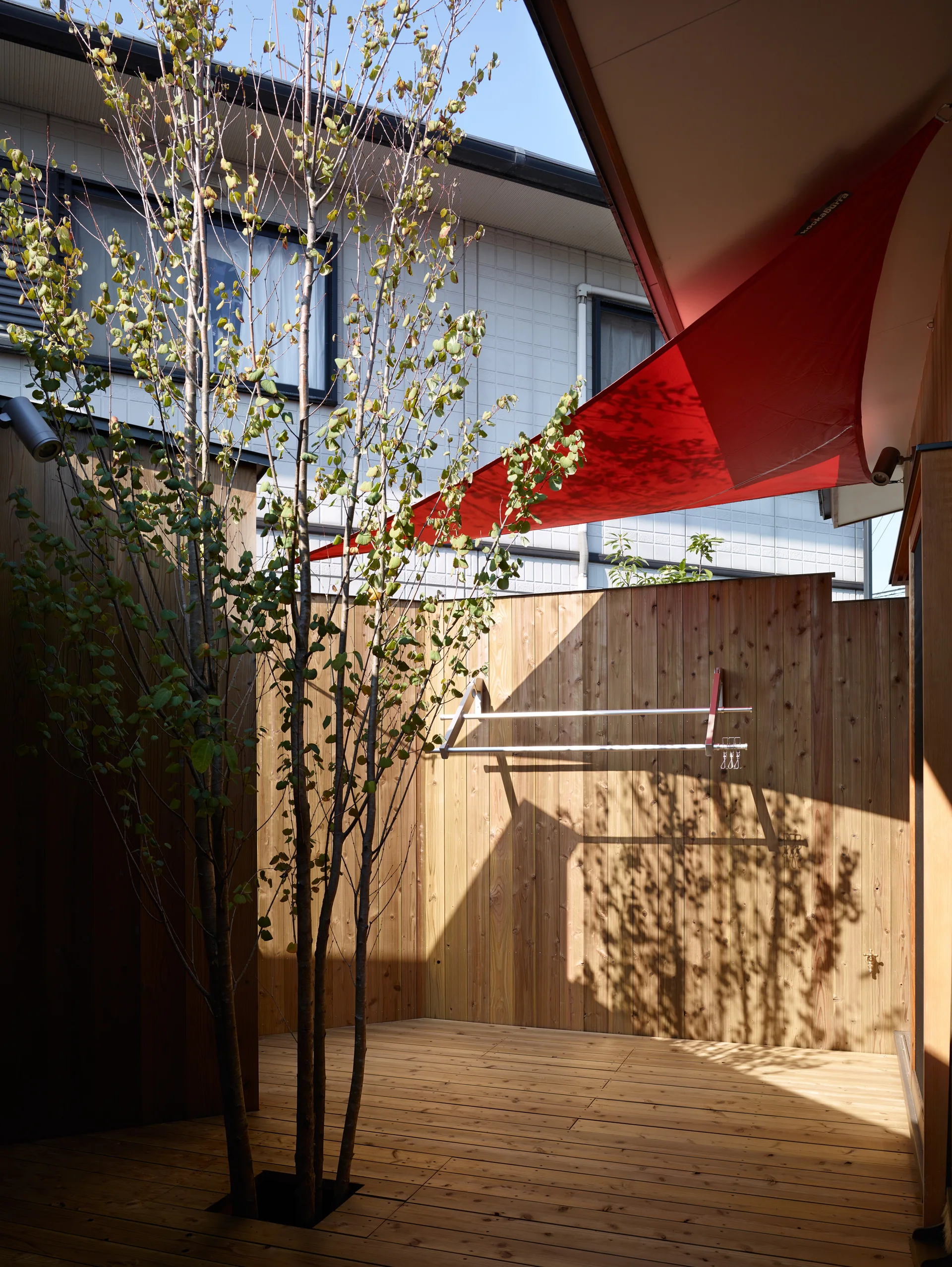 A private outdoor wood courtyard deck featuring a tree growing through a floor cutout and a red triangular sun shade sail overhead.