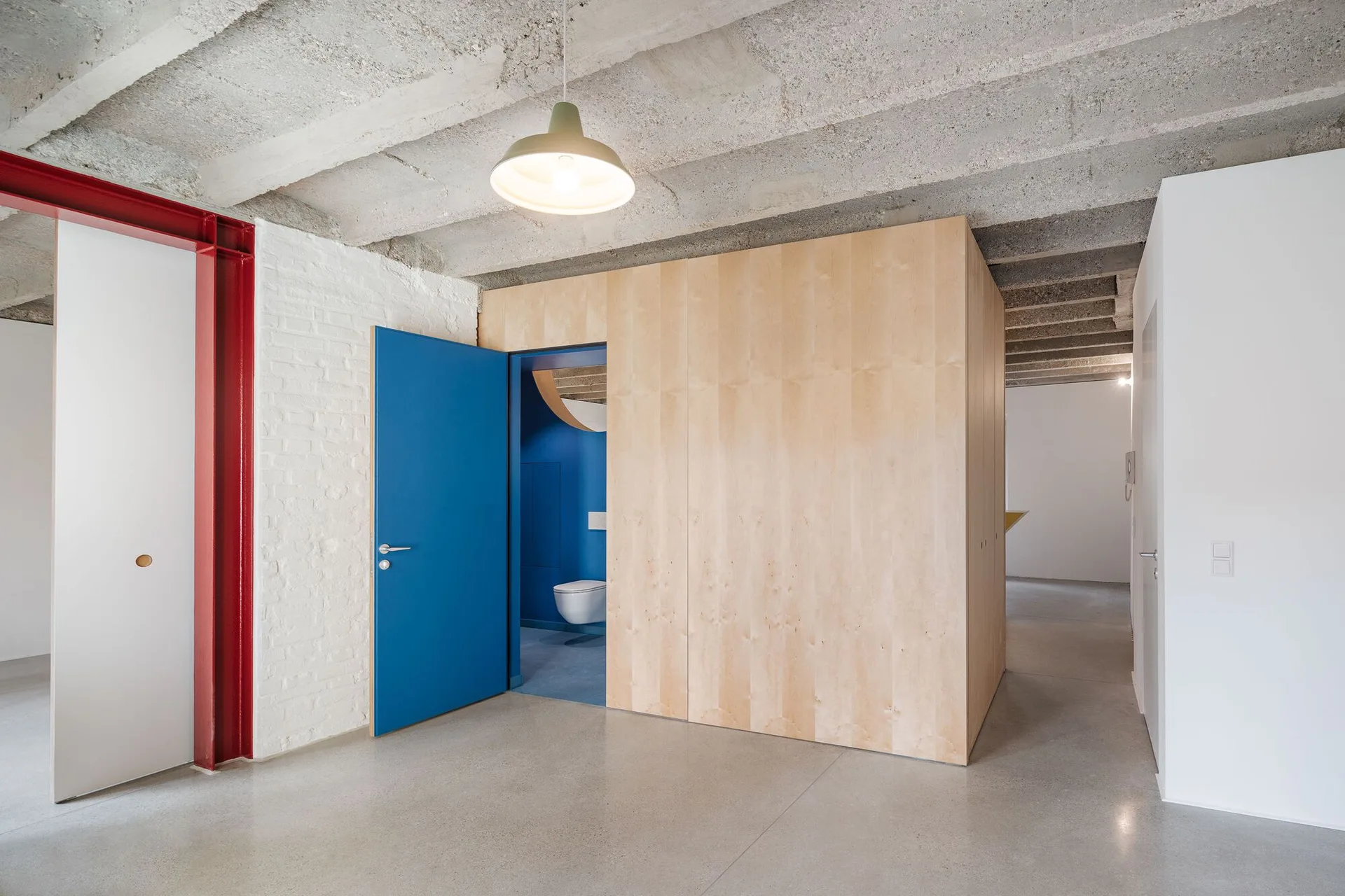 An open interior space featuring a light wood partition wall with an open blue door, polished concrete floors, and an exposed concrete ceiling.