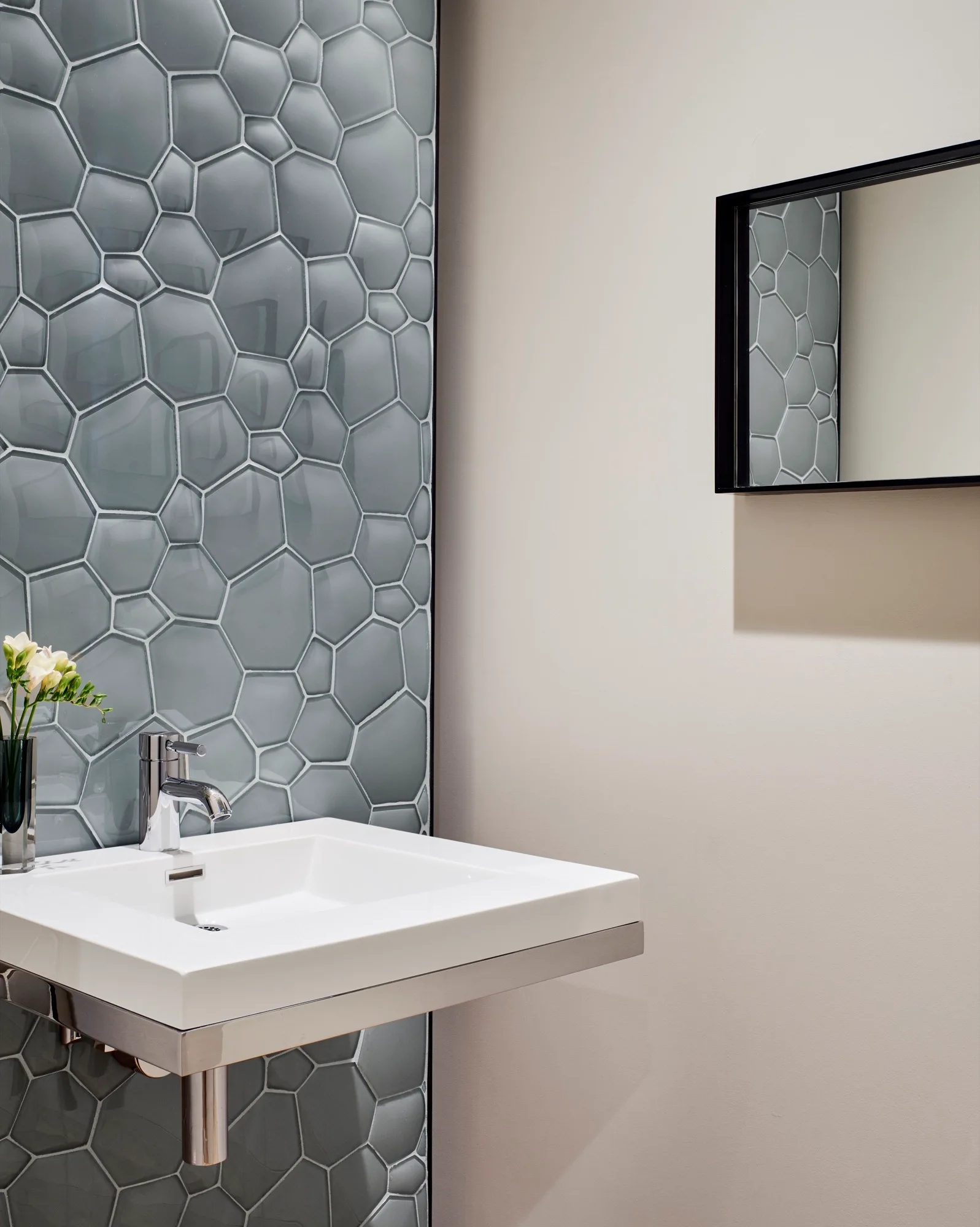 A modern wall-mounted white ceramic sink is set against a vertical feature strip of glossy grey hexagonal tiles.