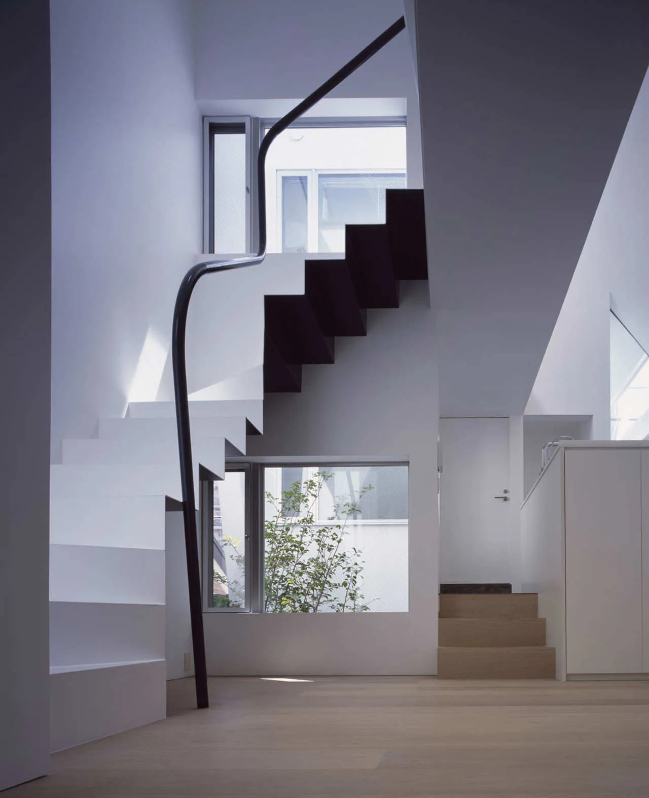 A minimalist modern staircase features white floating treads, a continuous black curved metal handrail, and light wood flooring.