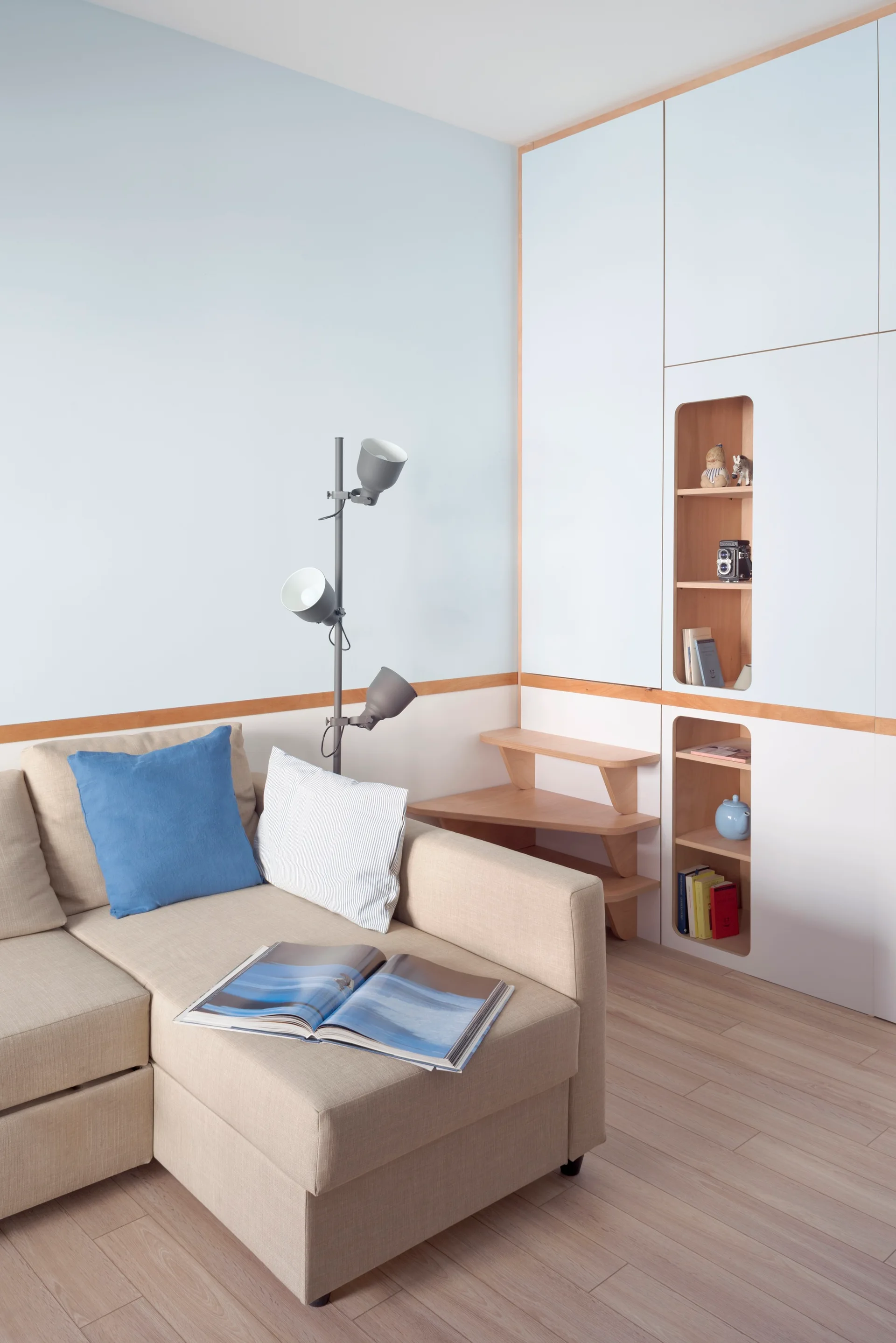 A beige sectional sofa sits next to a three-bulb floor lamp and a white built-in closet featuring recessed wood shelving.