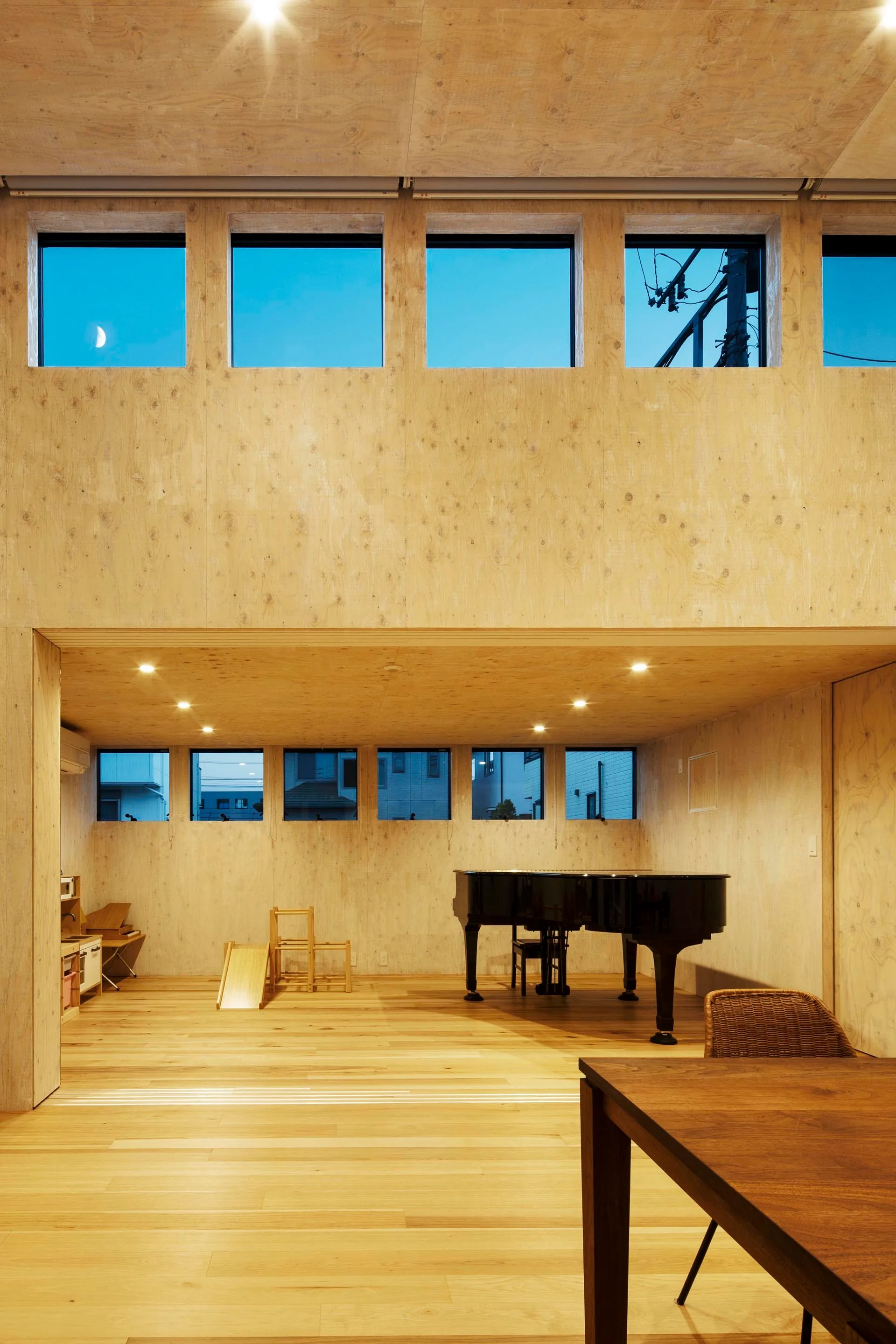 A minimalist room clad in natural plywood featuring a black grand piano on a light wood floor with a row of square windows.