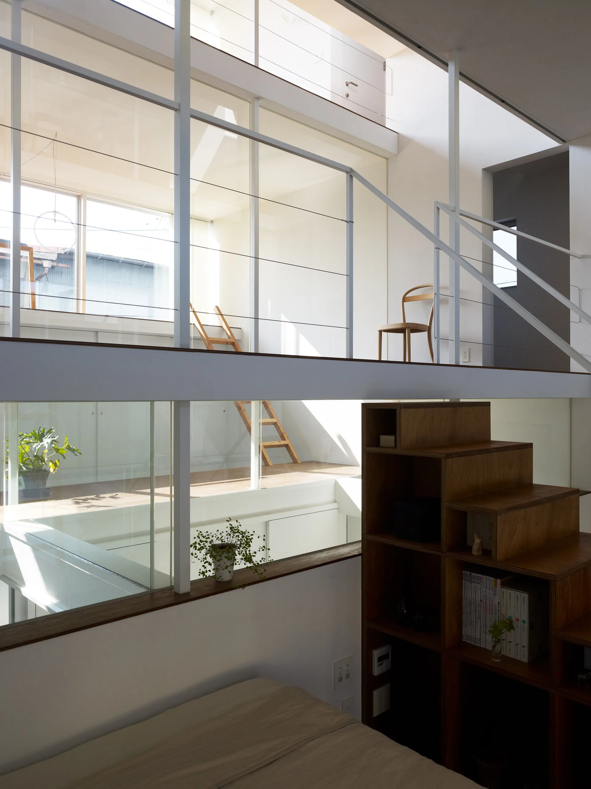 A modern multi-level home features a wooden storage staircase leading up to a sunlit mezzanine with a glass partition and white railings.