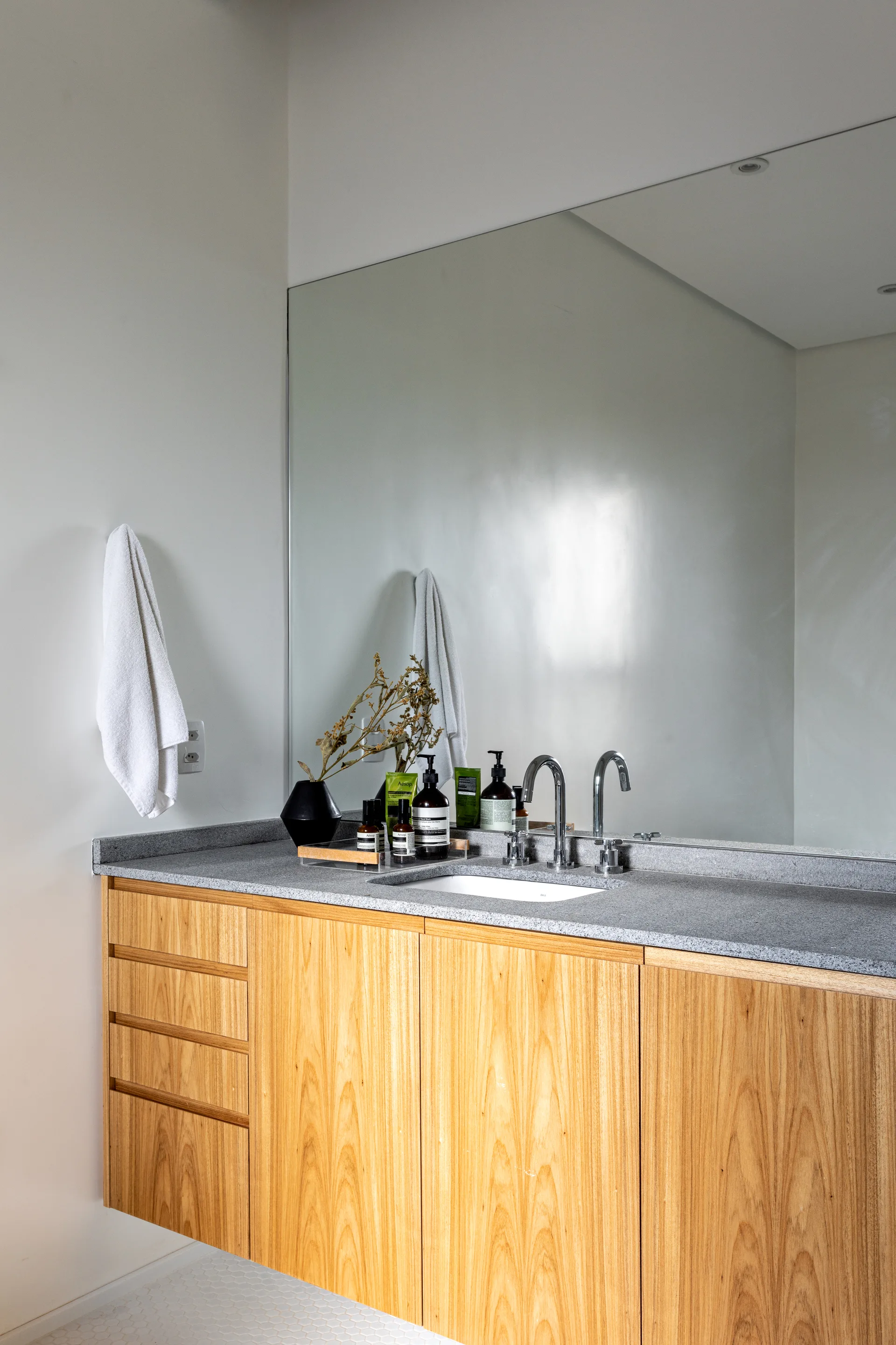 A floating natural wood bathroom vanity with a gray stone countertop, undermount sink, chrome faucets, and a large frameless wall mirror.
