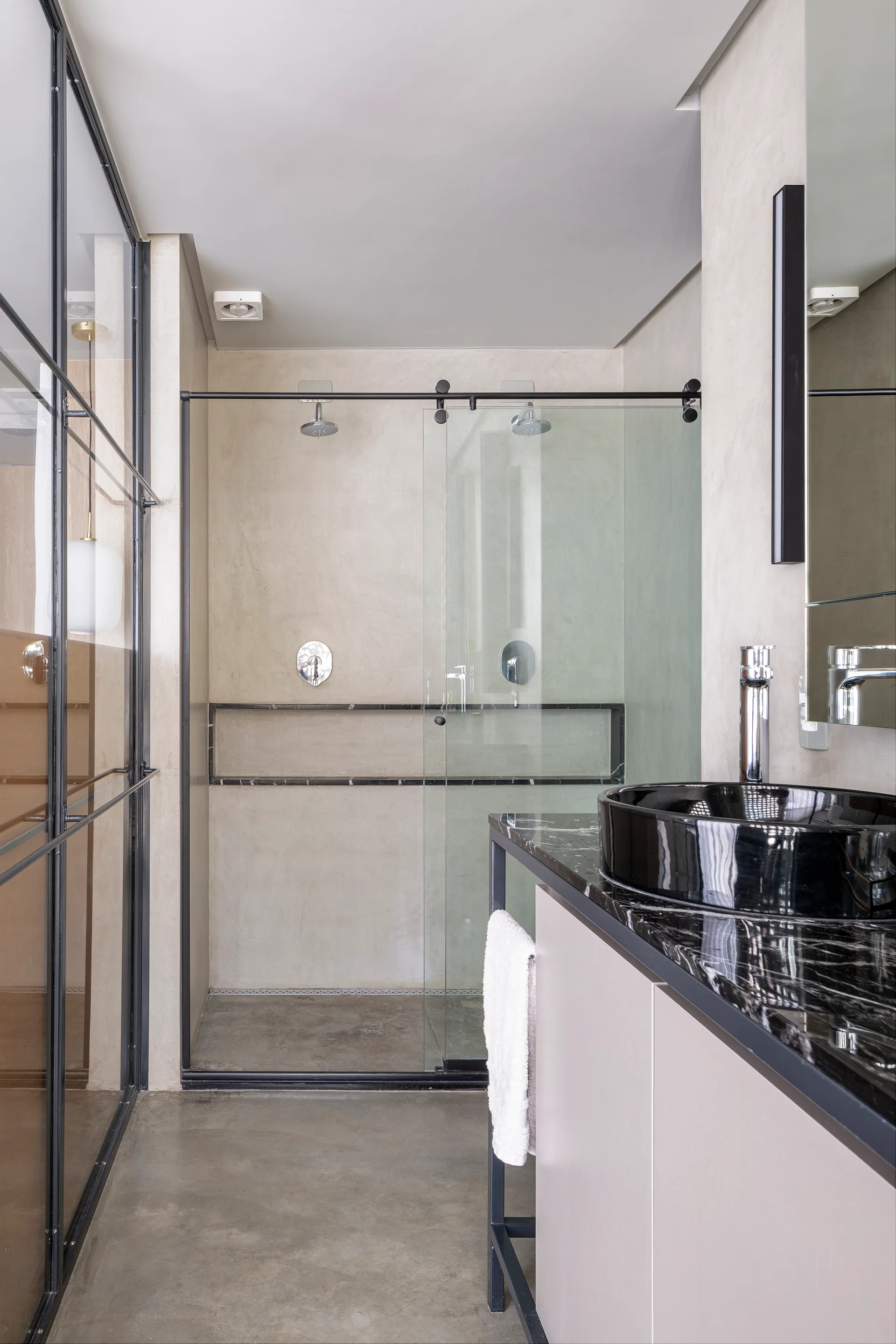 A modern bathroom featuring a black marble vanity with a glossy vessel sink and a glass-enclosed walk-in shower against textured plaster walls.