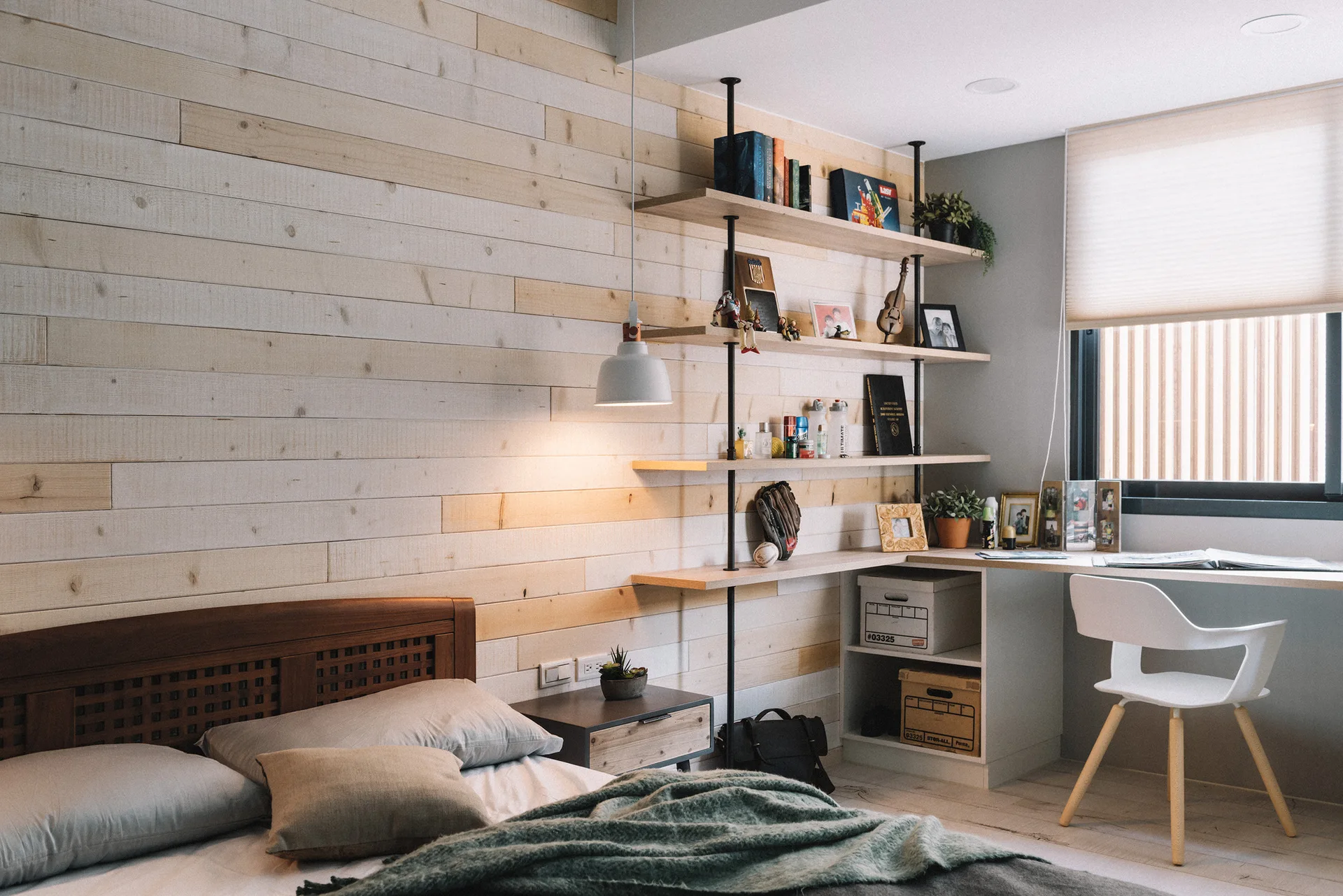 A modern bedroom featuring a light wood plank accent wall, a platform bed with gray bedding, and a white integrated desk with open shelving.