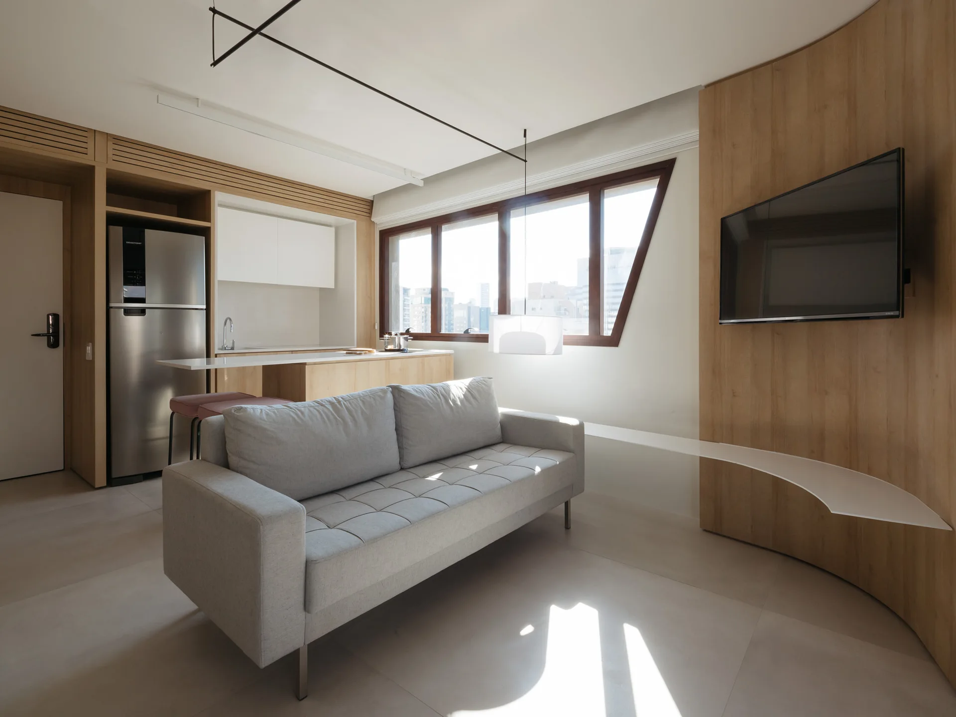 A modern open-plan living room featuring a grey tufted sofa, integrated wood kitchen cabinets, and a curved wood-paneled TV wall.