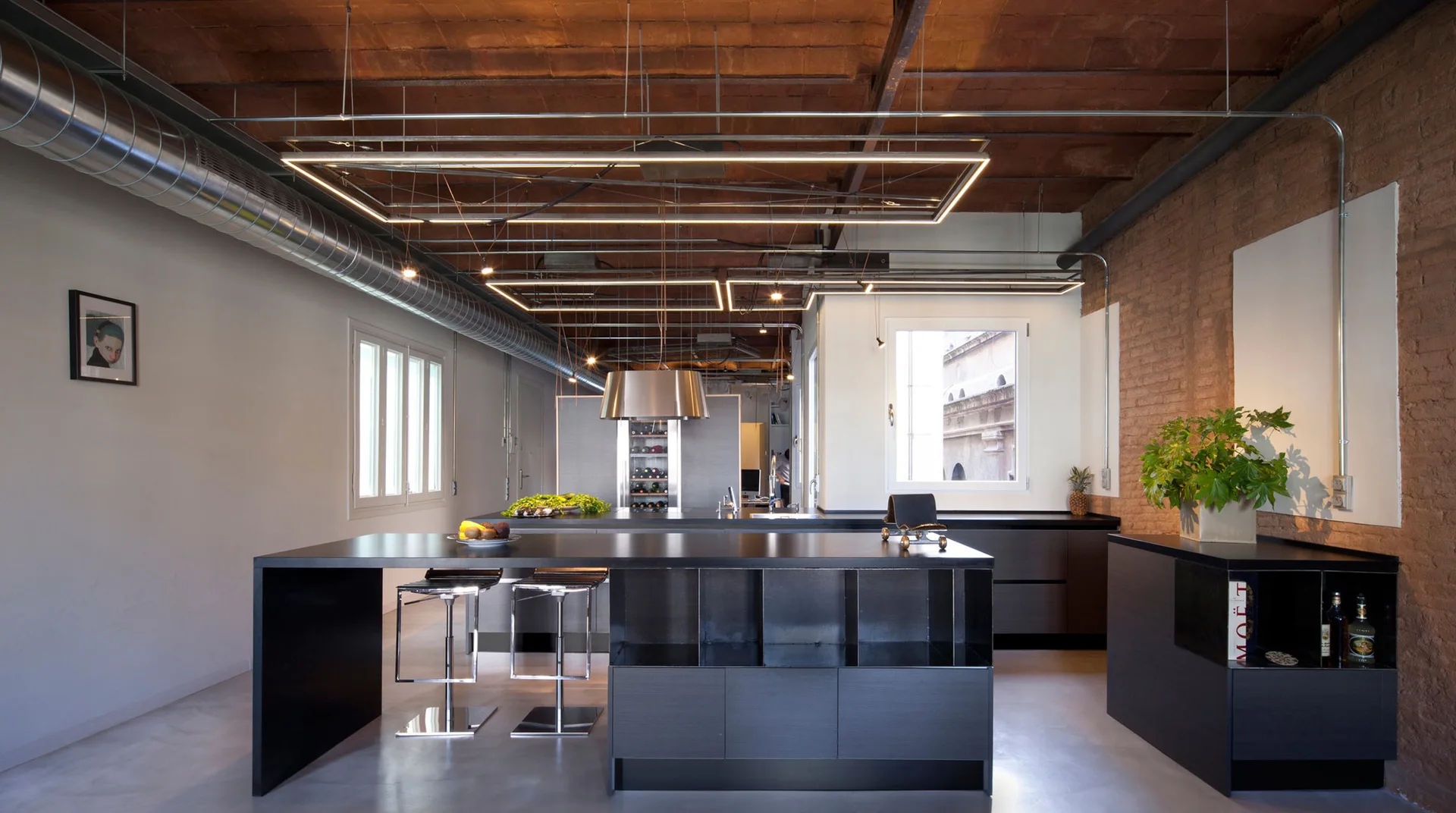 An industrial loft kitchen features a black island with bar stools, a vaulted brick ceiling, linear LED light fixtures, and polished concrete floors.