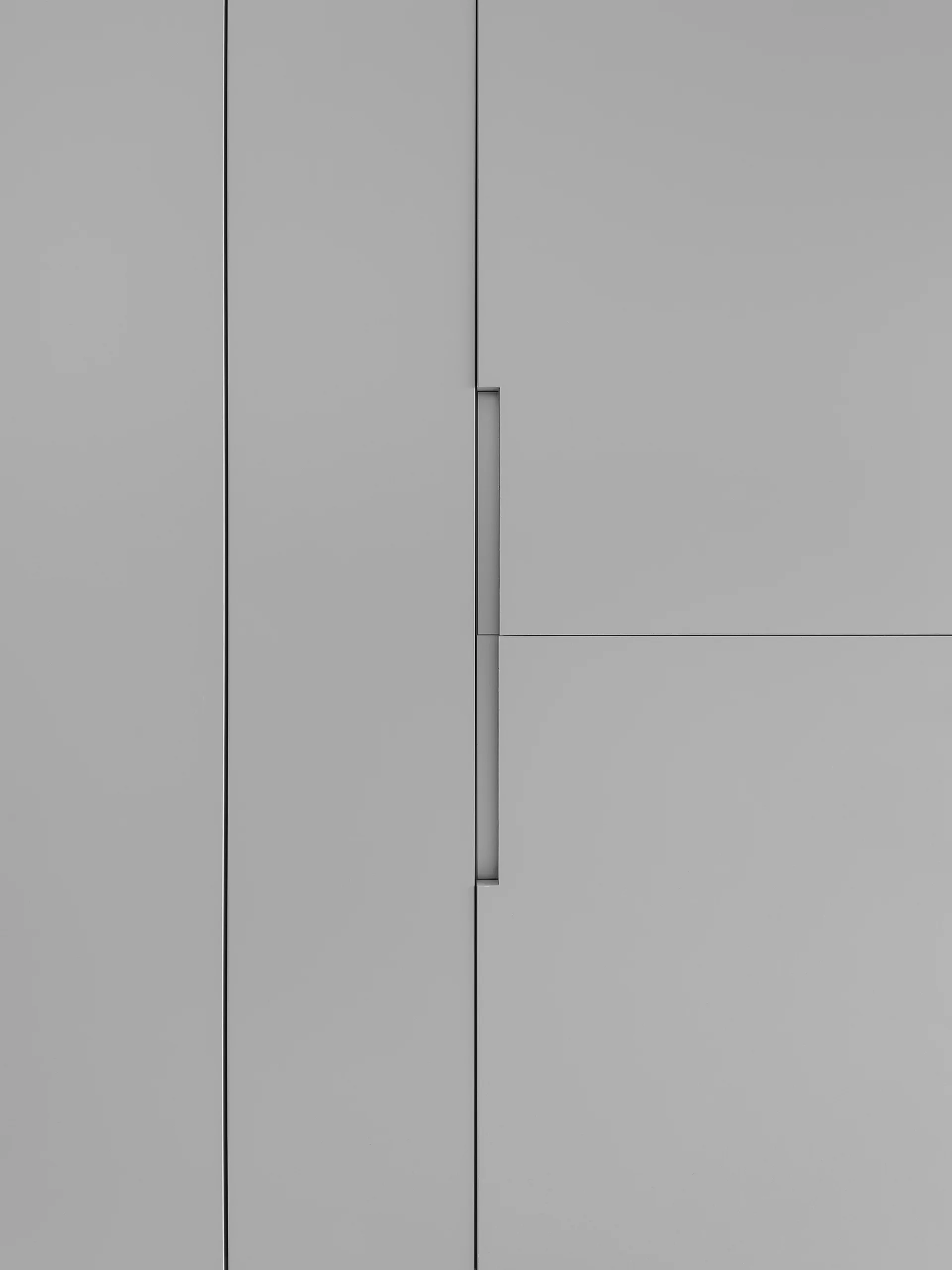 A close-up view of minimalist matte grey cabinet doors featuring vertical integrated recessed handles and clean panel seams.