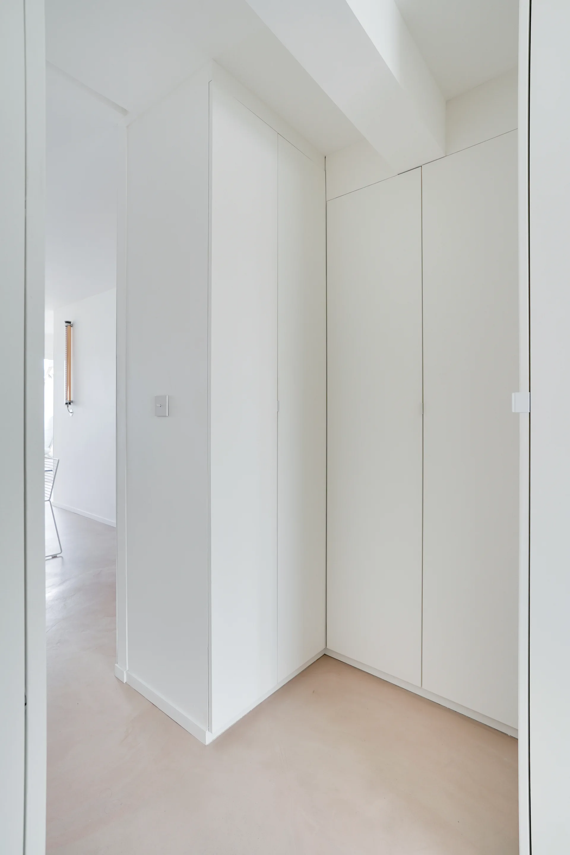 A minimalist white hallway features handleless built-in cabinetry and smooth light-toned matte flooring.