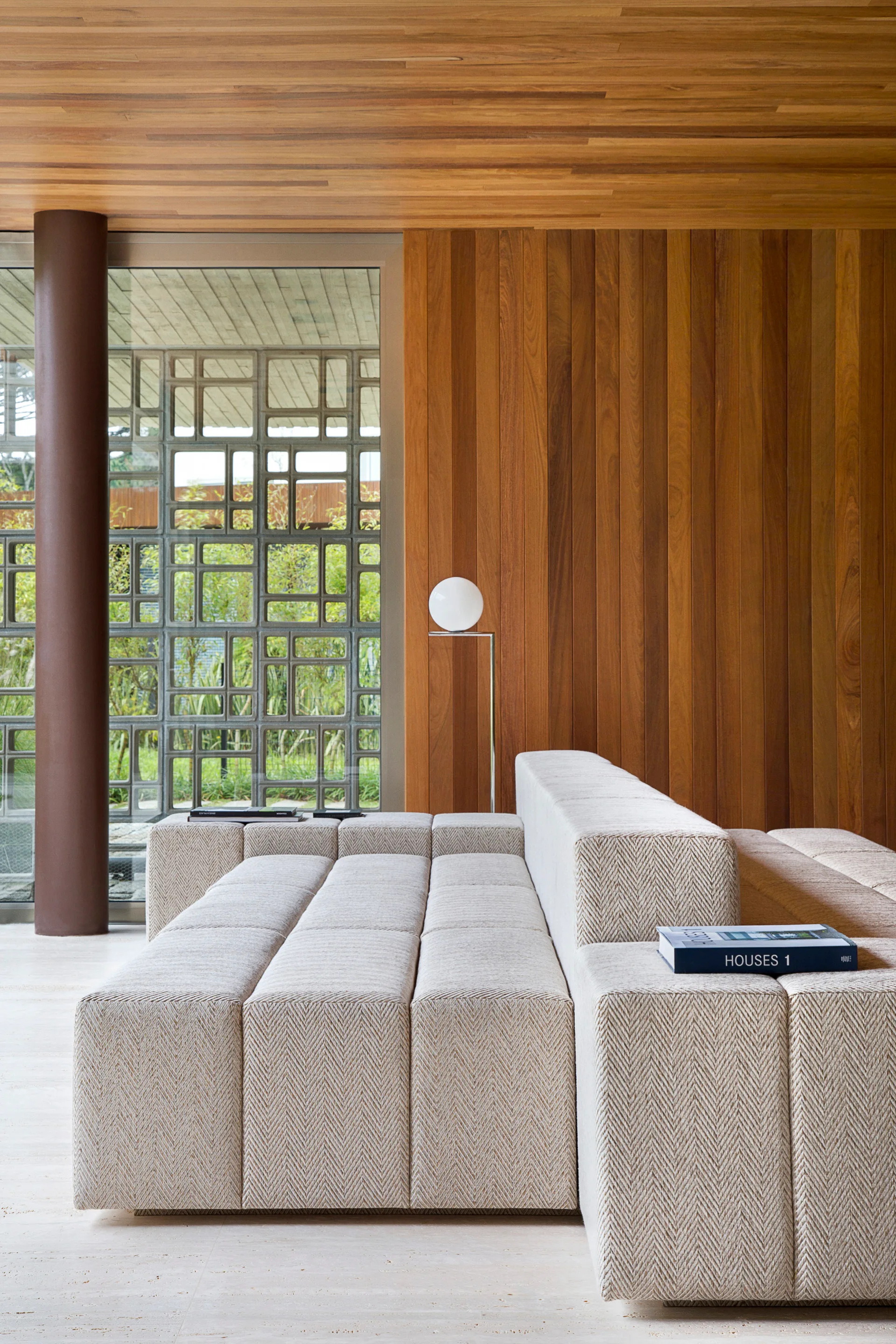 A low-profile modular beige sectional sofa is set against a backdrop of rich vertical wood wall paneling and a matching wooden plank ceiling.