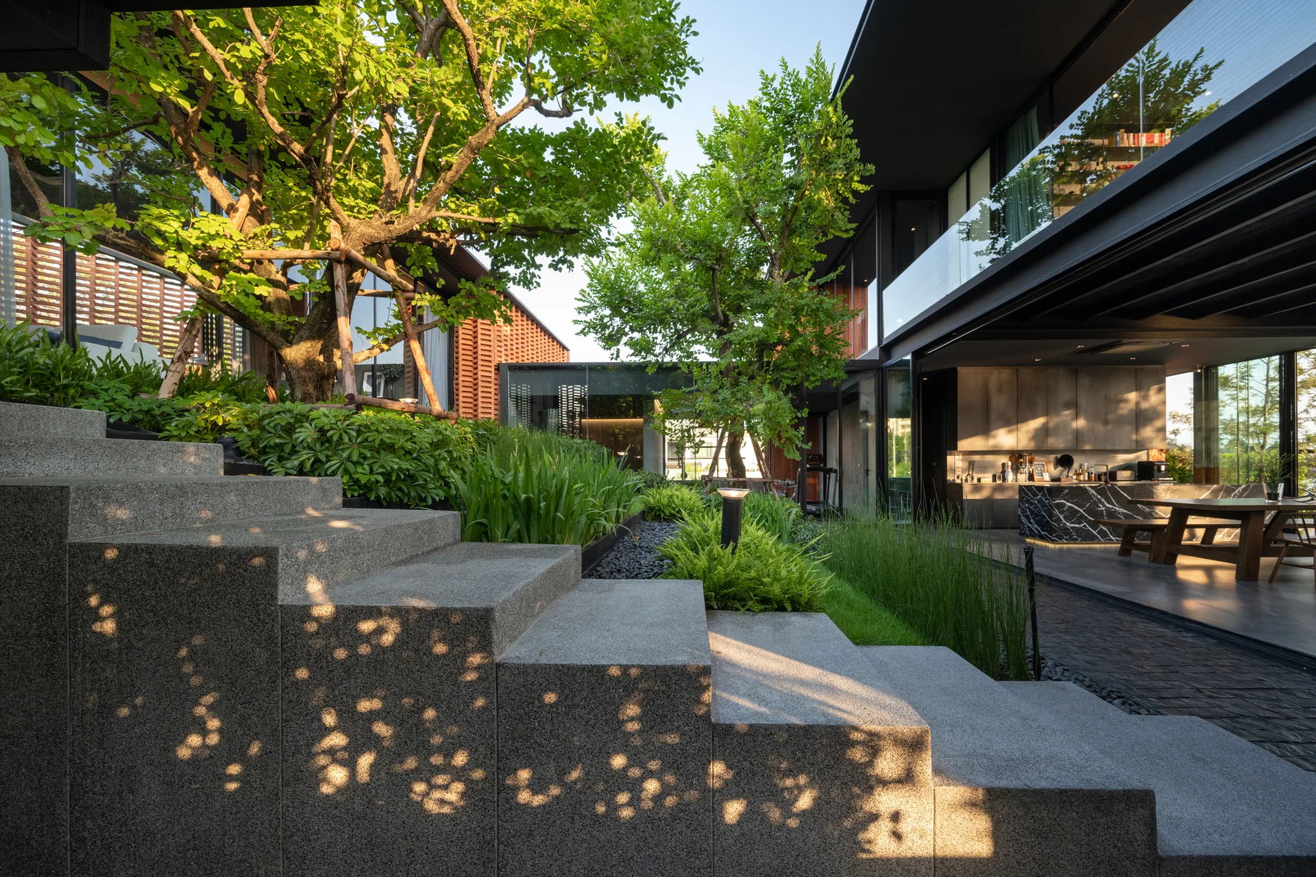 Concrete outdoor steps overlook a landscaped courtyard garden next to an open kitchen with a black marble island.