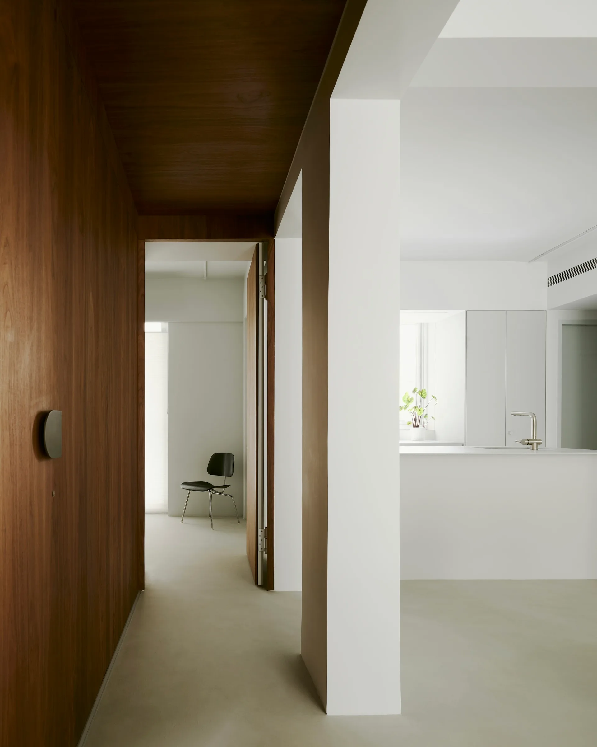 A hallway with warm wood paneling on the walls and ceiling leads to a bright white kitchen with a minimalist faucet.