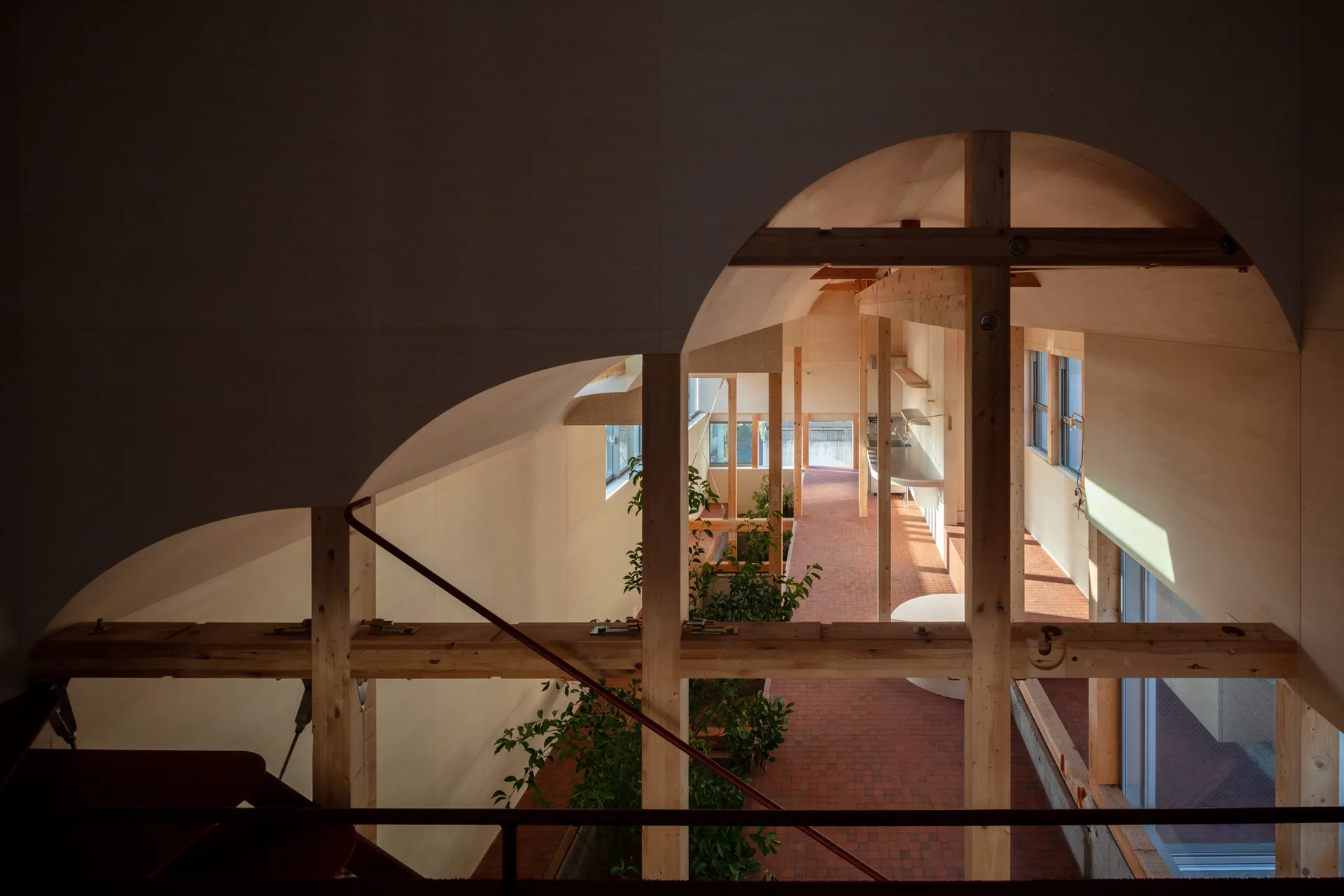 An elevated view of a modern residential interior featuring exposed timber columns, an arched plywood ceiling, and terracotta tile floors.