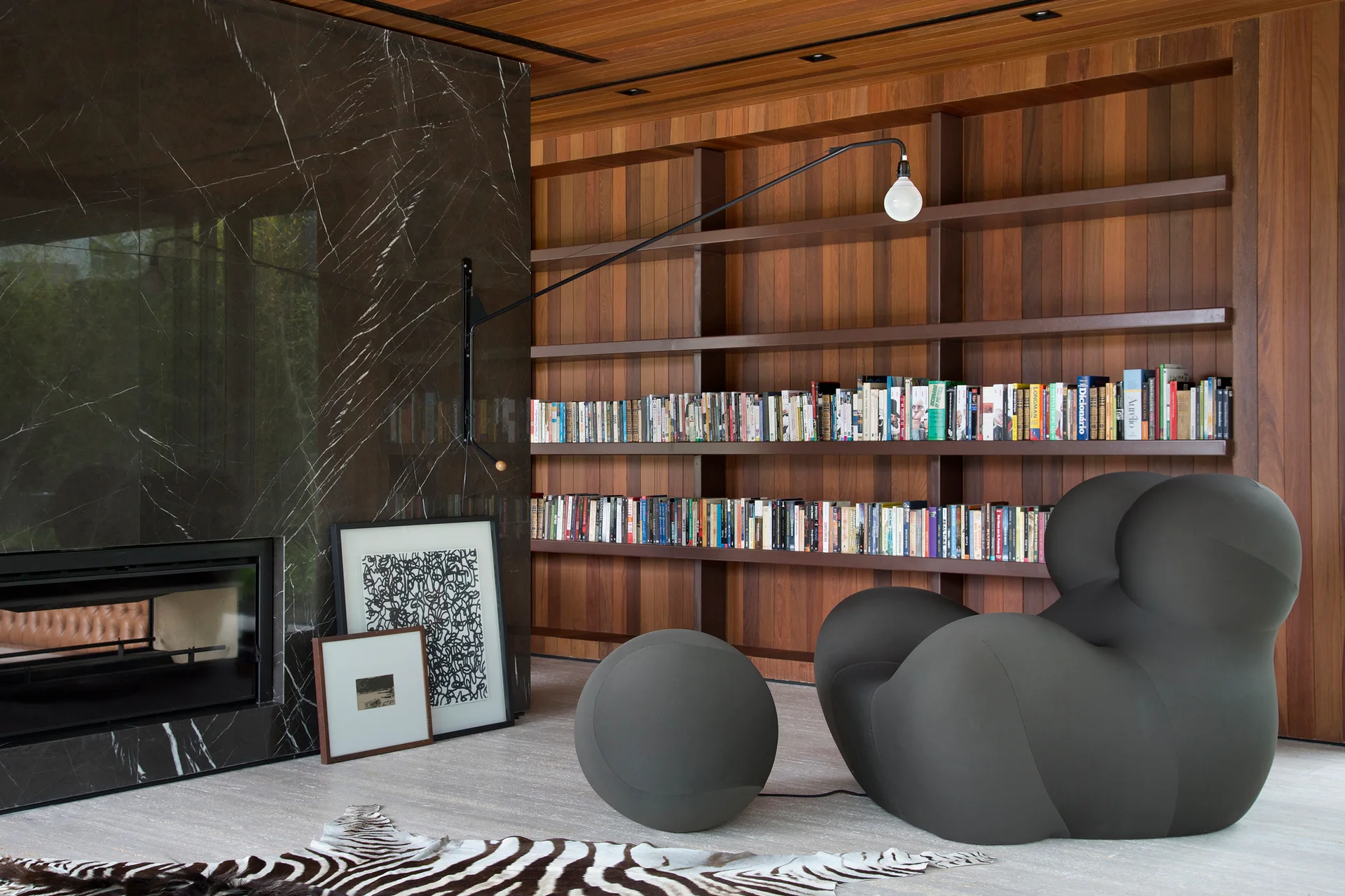 A contemporary living area with a dark marble fireplace, a built-in wooden library wall, a sculptural dark grey armchair, and an animal print rug.