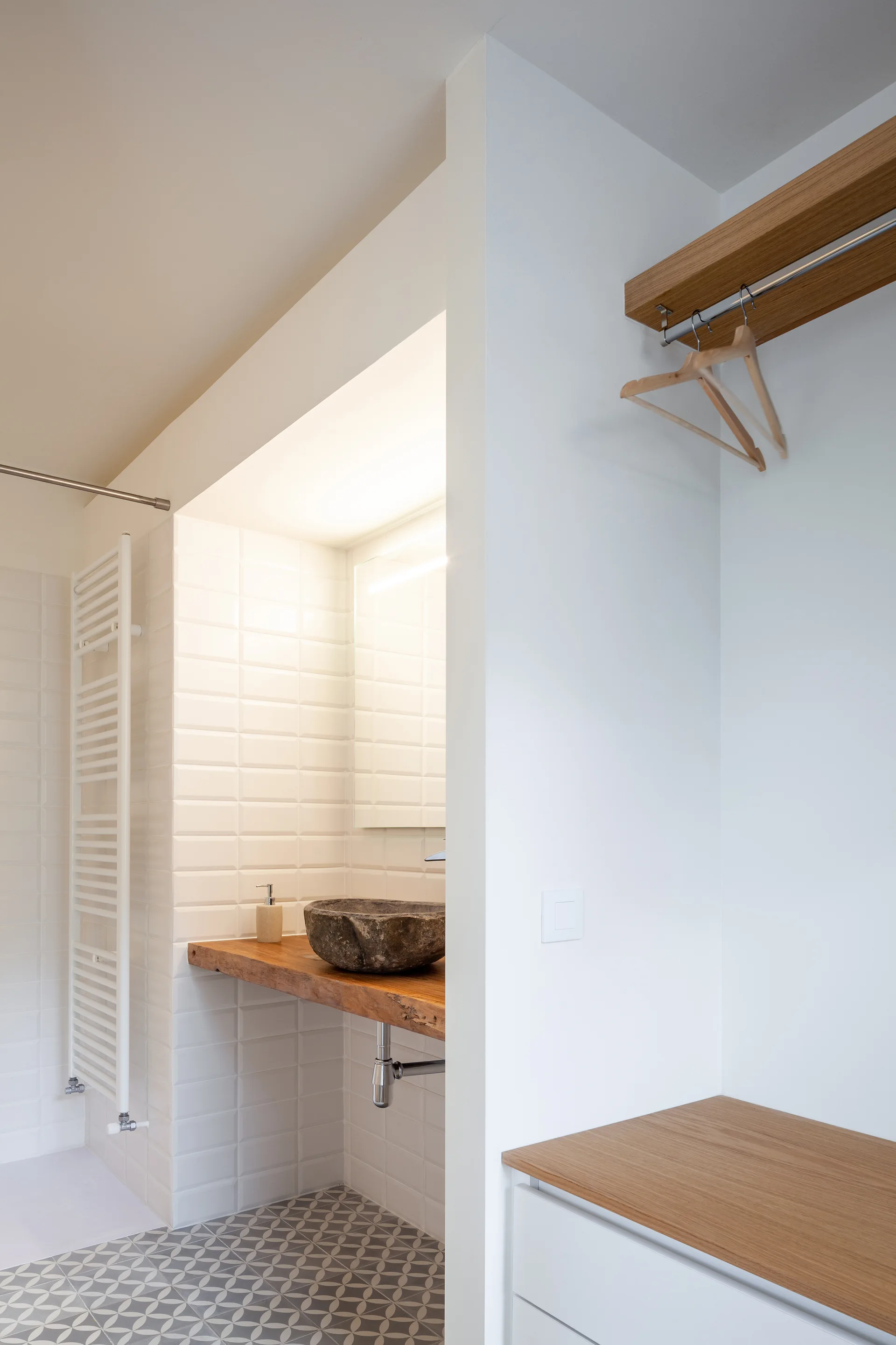 A modern bathroom showcases a stone vessel sink on a thick wood counter next to an open closet area with matching light wood shelving.