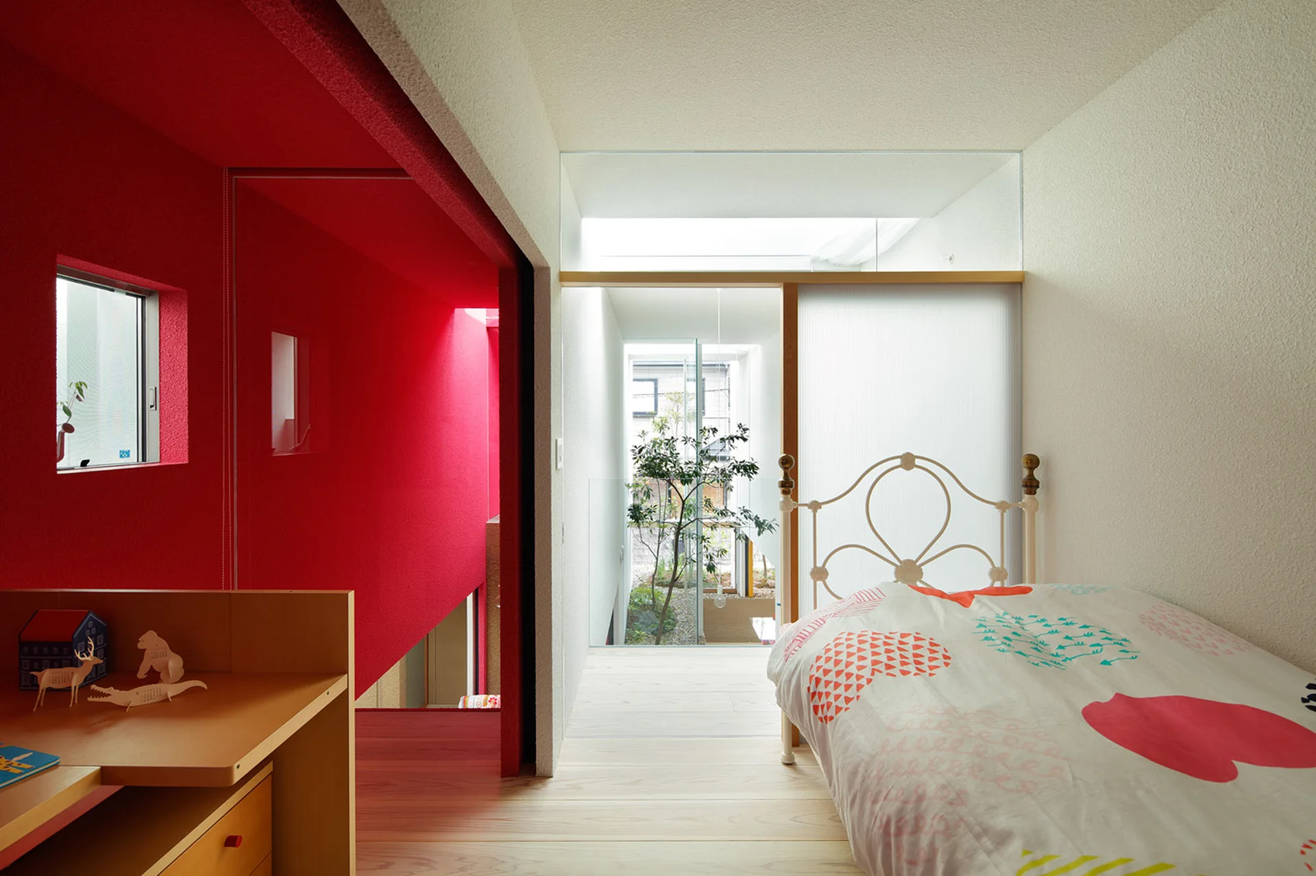 A minimalist bedroom with a metal bed, light wood floors, a bold red wall, and a translucent sliding screen leading to an interior courtyard.