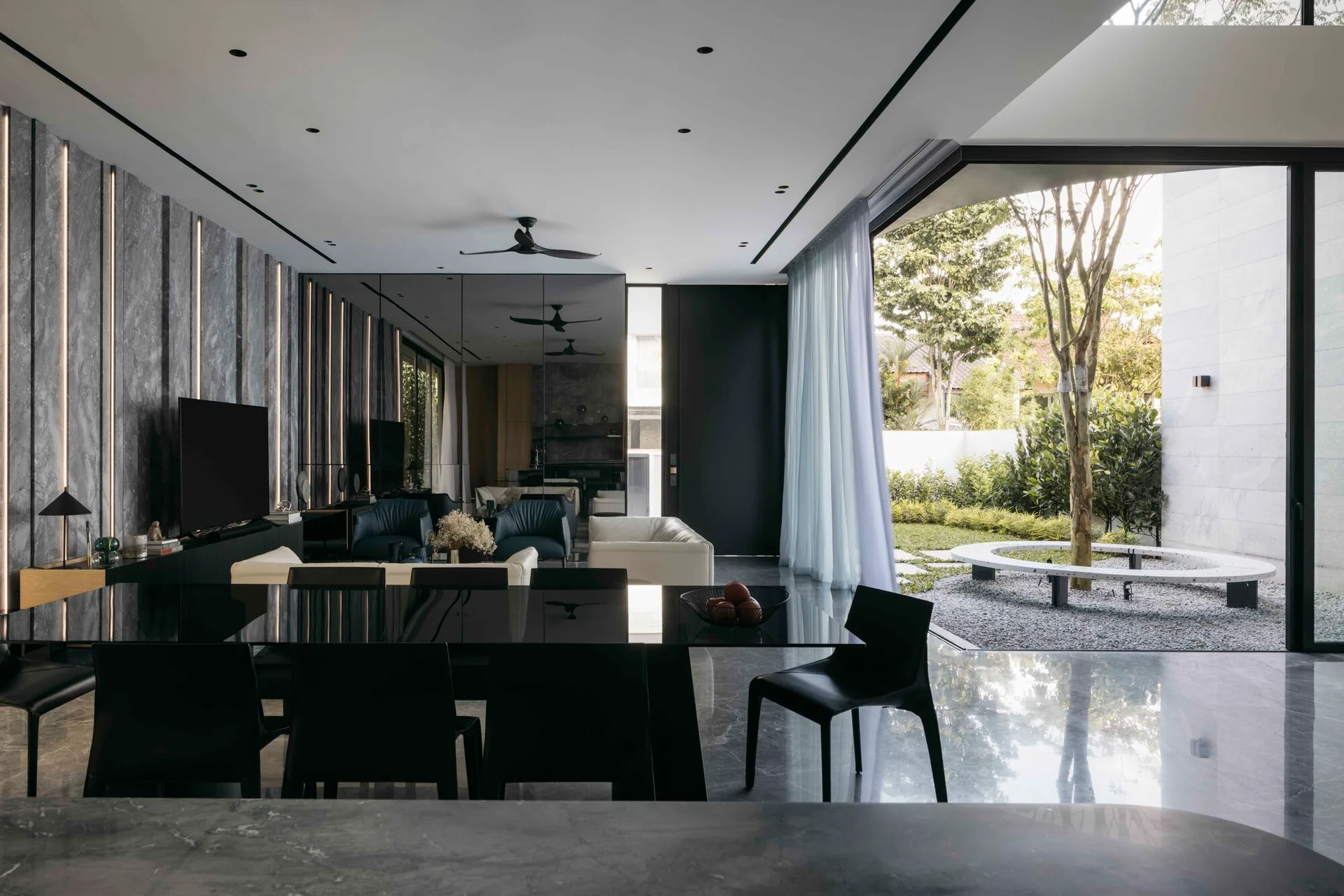 A modern monochromatic open-plan living and dining room with a large sliding glass wall opening onto an outdoor courtyard with a tree.