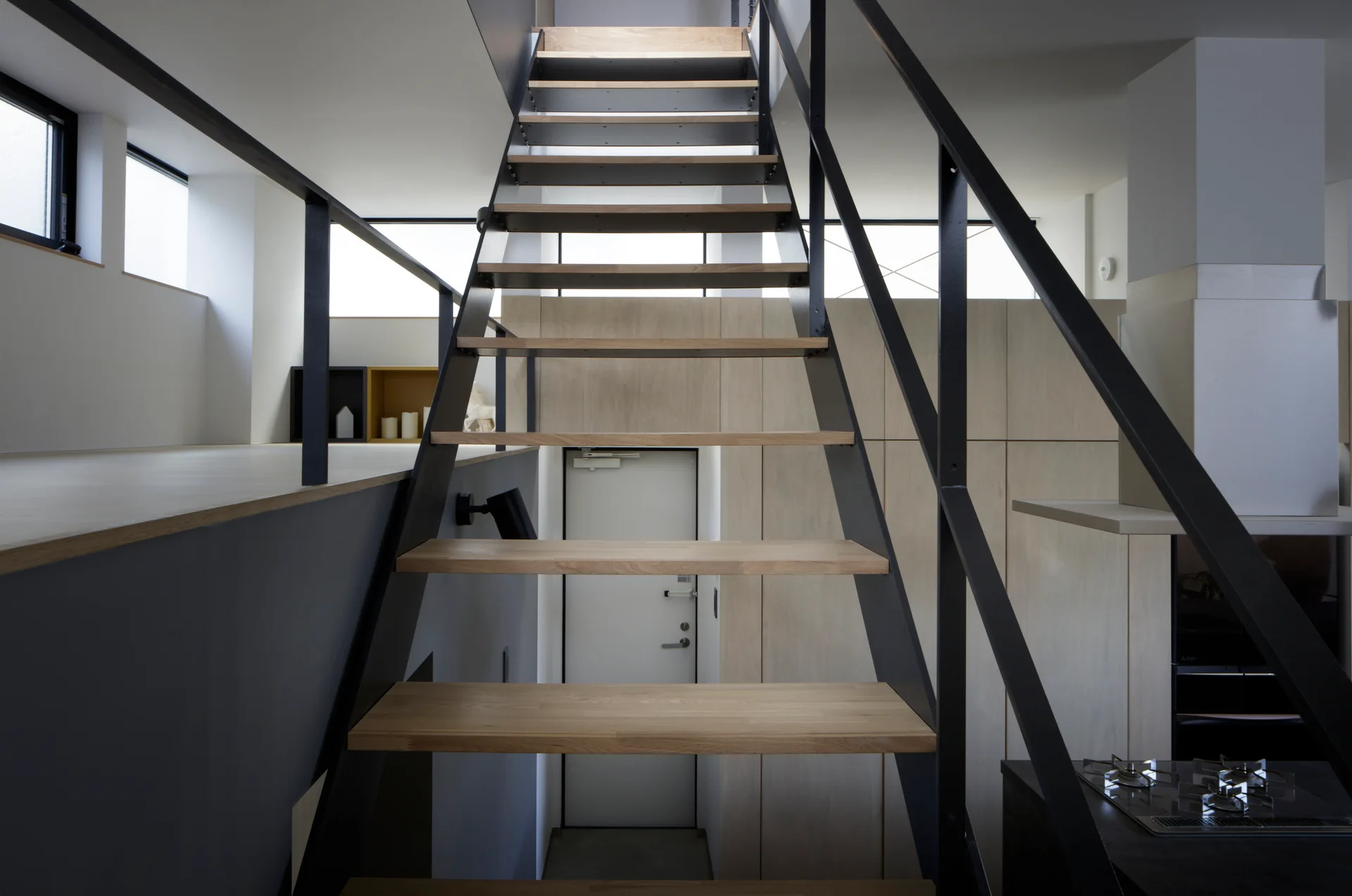 An open-riser staircase with light wood treads and black metal railings connects split levels in a minimalist modern home.