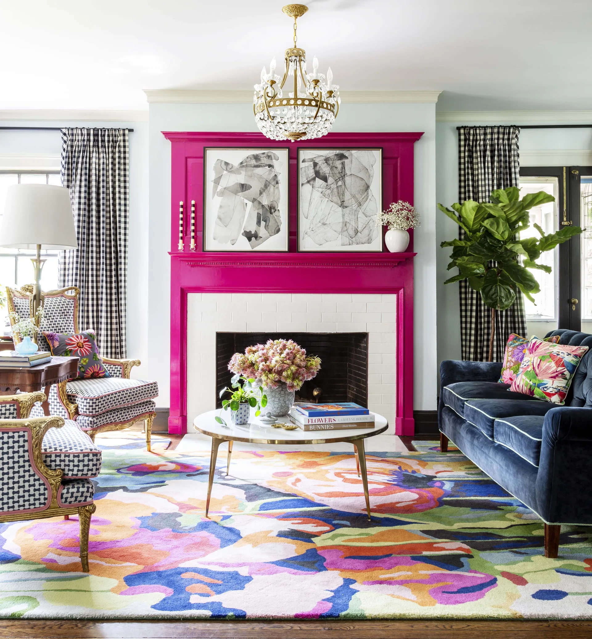 An eclectic living room featuring a hot pink fireplace mantle, a blue velvet sofa, a colorful floral rug, and gingham curtains.