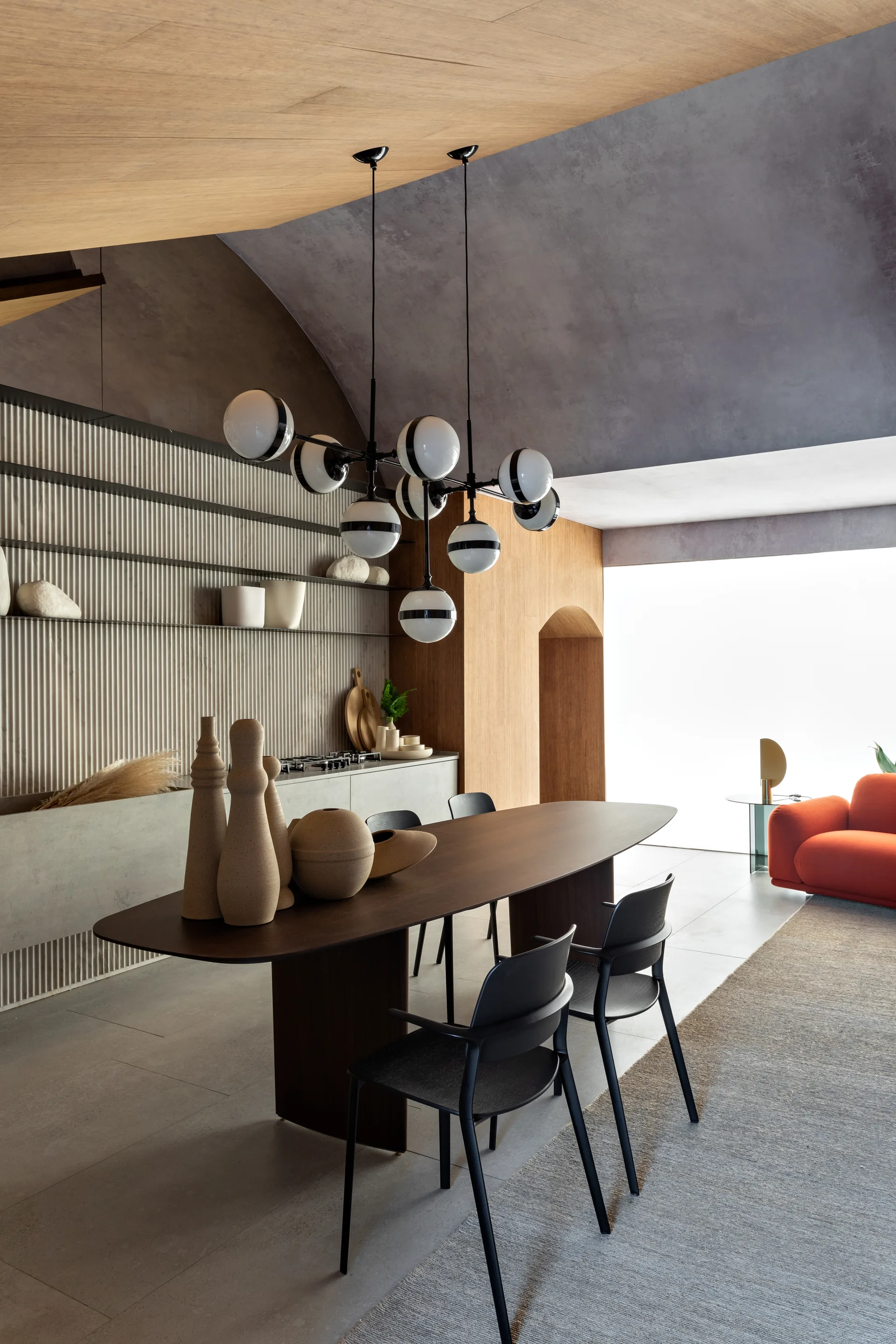 A modern dining room featuring a dark wood oval table, black chairs, and a sculptural multi-globe chandelier against a grey fluted accent wall.