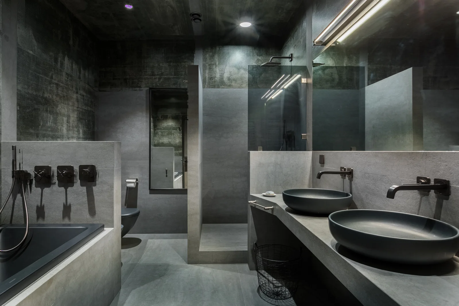 A modern gray concrete bathroom featuring a double vanity with two black vessel sinks, a matching bathtub, and an integrated walk-in shower.