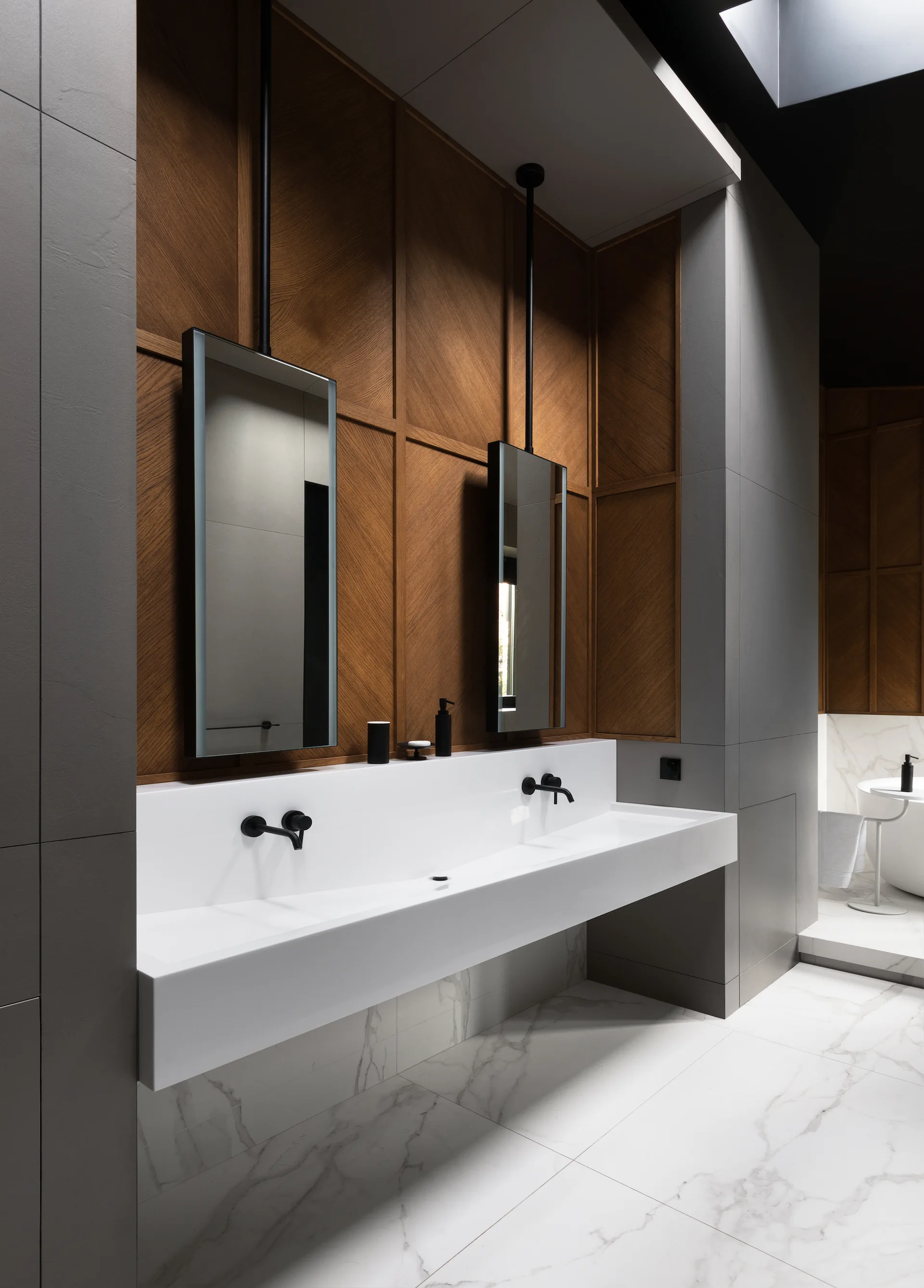 A modern bathroom features a floating white double vanity with black faucets against wood paneling, grey tile walls, and hanging rectangular mirrors.