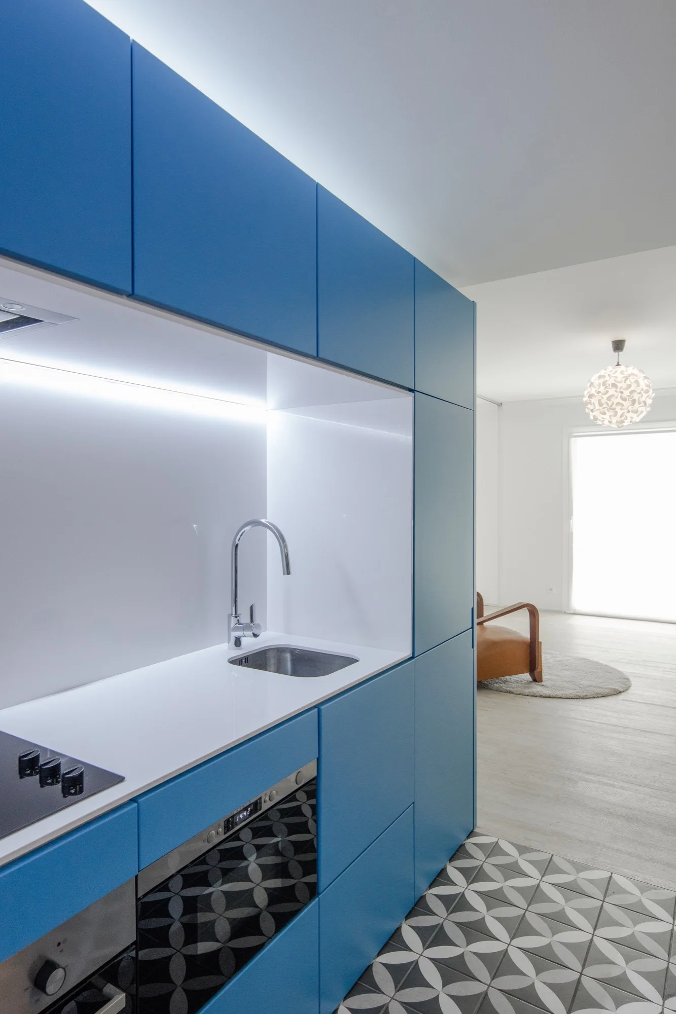 Modern kitchen featuring matte blue flat-front cabinets, a white recessed workspace, integrated under-cabinet lighting, and geometric patterned floor tiles.