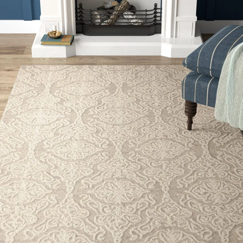 A tan damask patterned area rug on a wood floor next to a blue striped armchair and a white fireplace hearth.