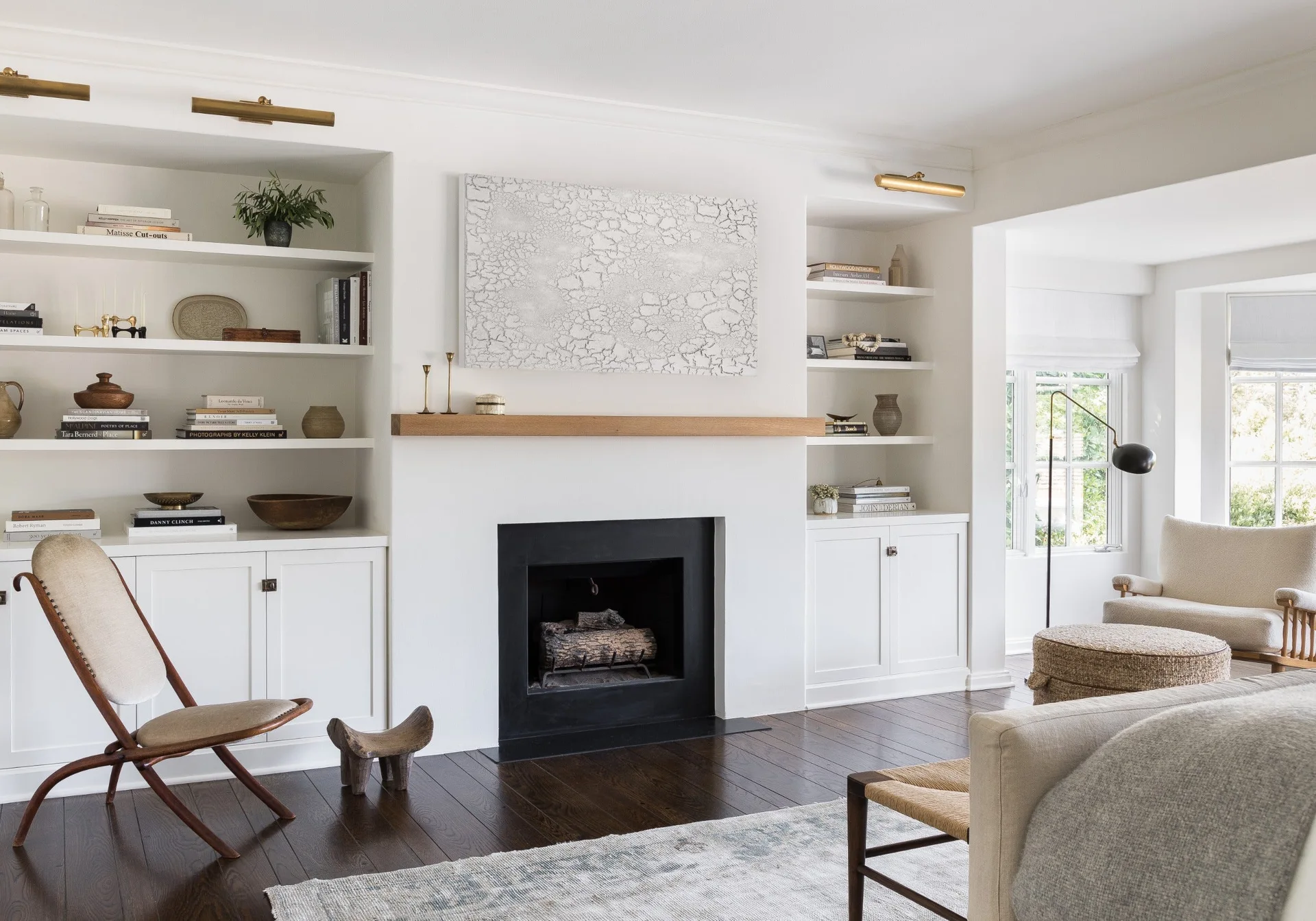 A living room fireplace featuring a natural wood mantel and flanking white built-in bookshelves styled with books, vases, and brass picture lights.