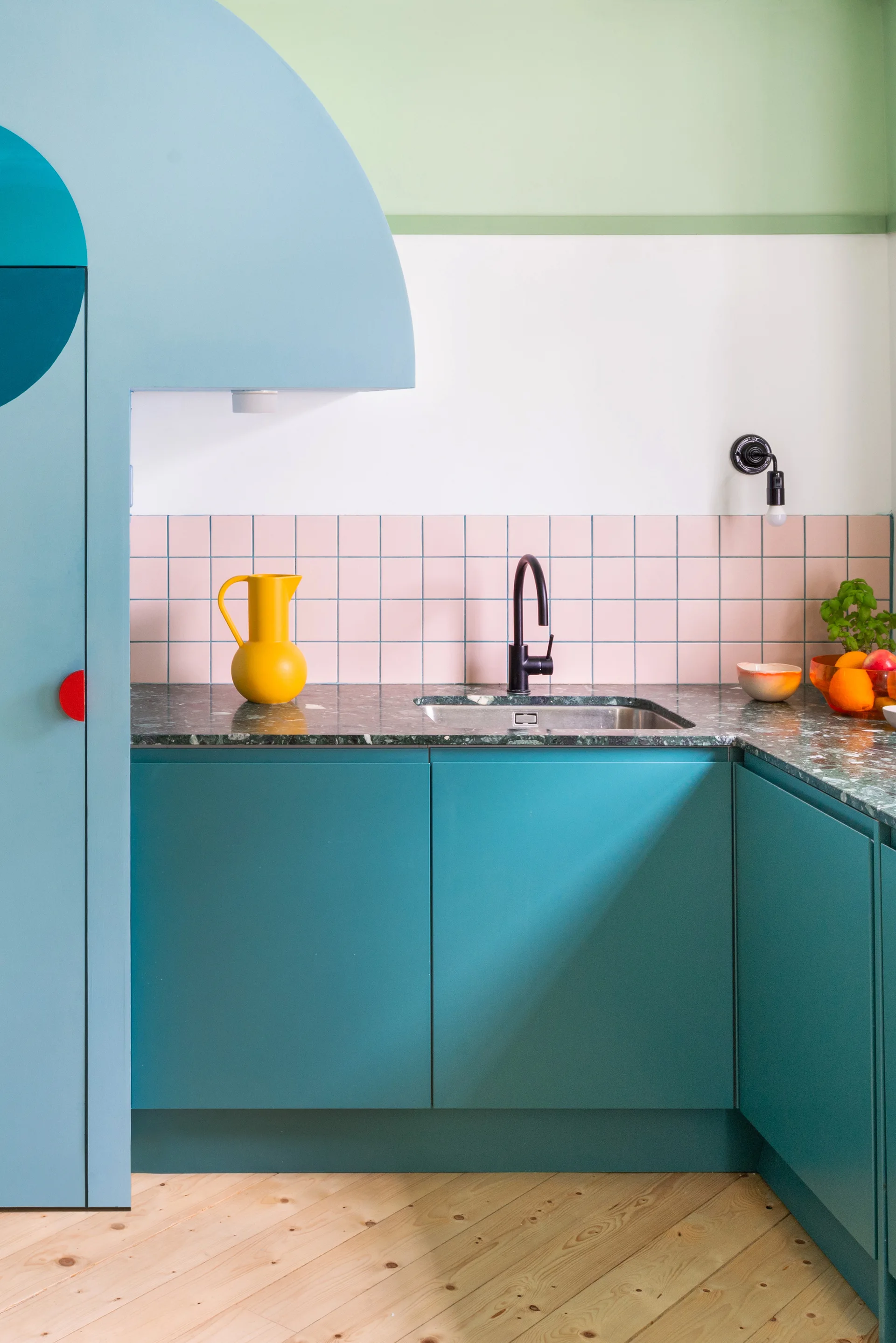 A kitchen corner features teal blue cabinets, a green stone countertop with an under-mount sink, and a pale pink square tile backsplash.