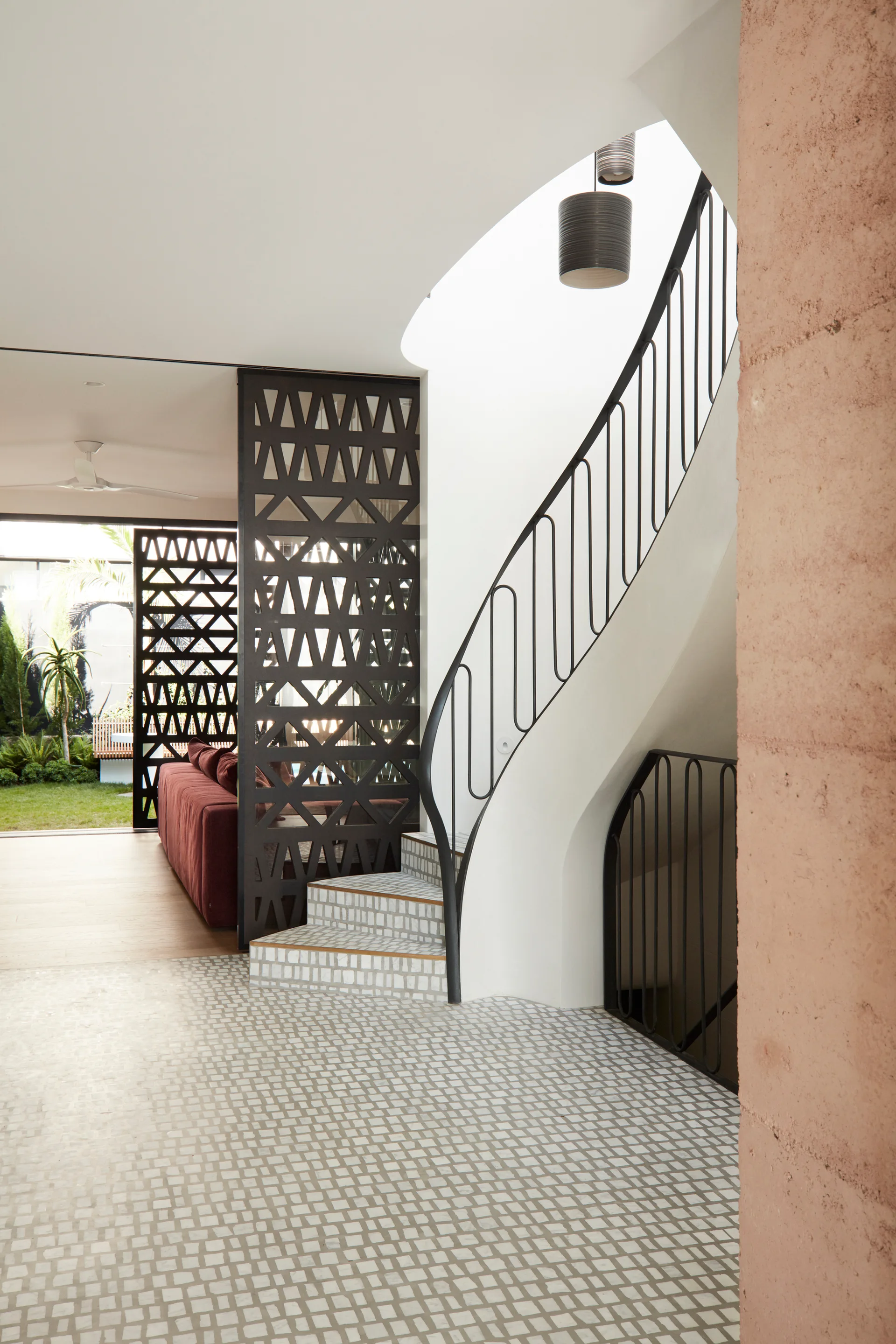 A modern entryway features a curved white staircase with a black metal railing, grey mosaic floor tiles, and a dark geometric lattice room divider.