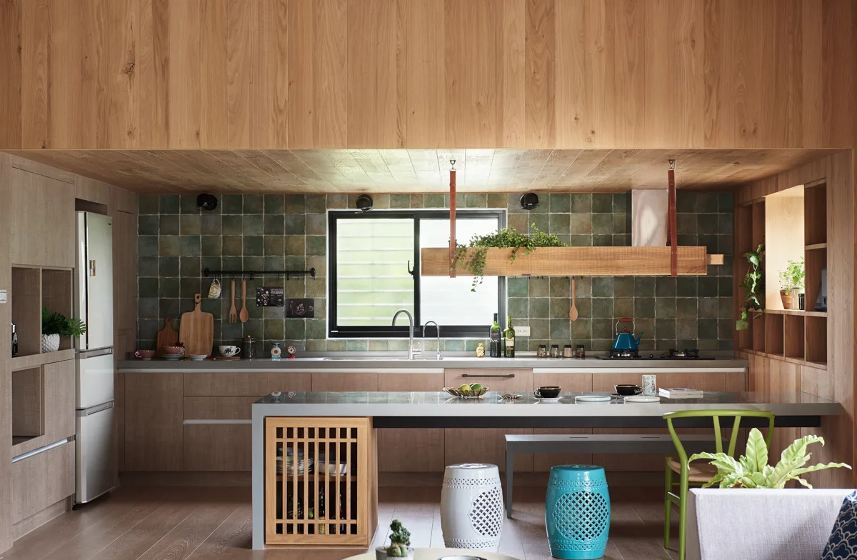 A wood-paneled kitchen features a green square tile backsplash, a long island with ceramic garden stools, and a hanging wooden planter.