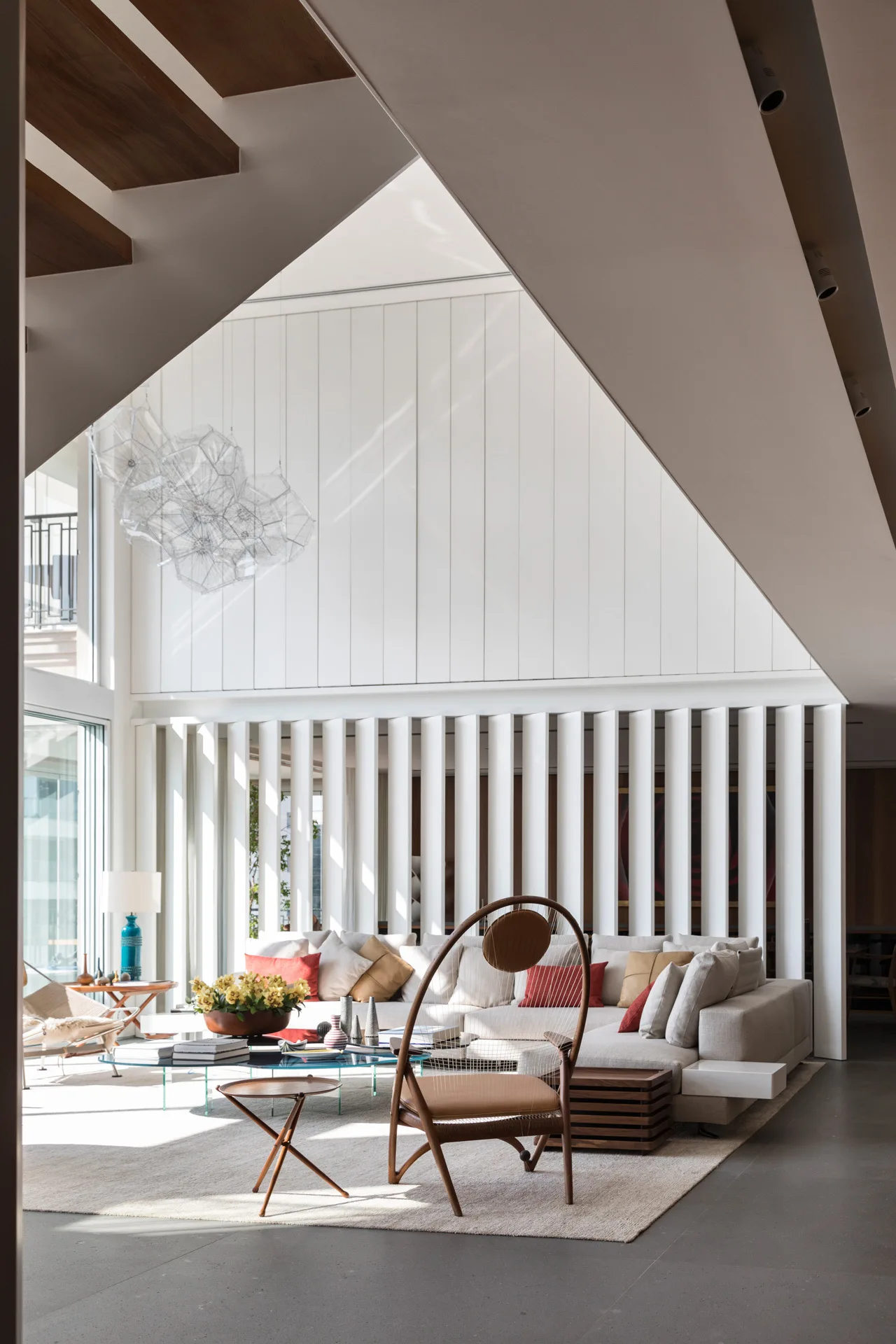 A bright contemporary living room featuring a beige modular sofa, a curved wood accent chair, and a white vertical slatted room divider.