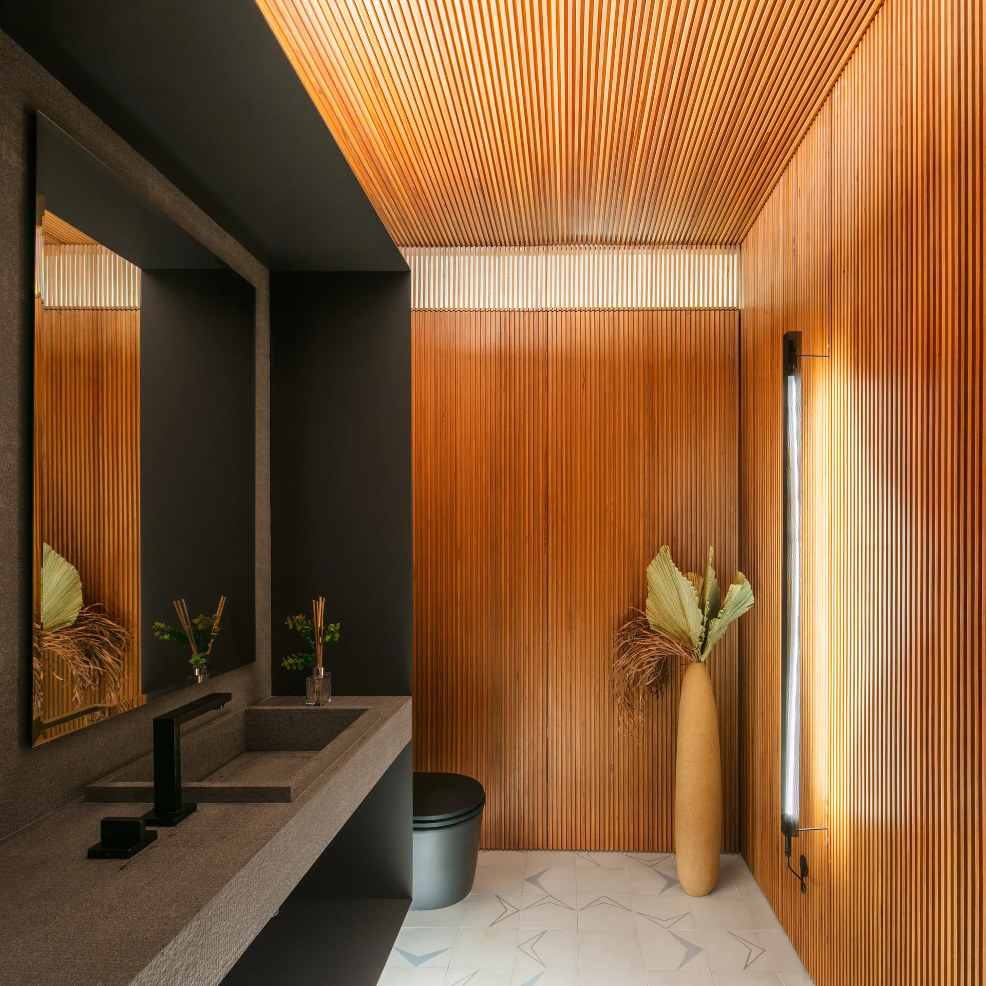 A contemporary powder room with vertical wood slat walls and ceiling, a dark stone vanity, and a black toilet.