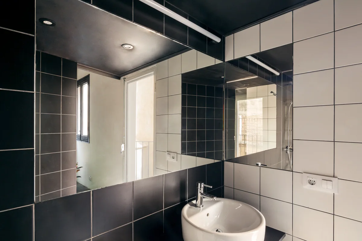 A modern bathroom corner features a white ceramic sink on a black vanity below a large mirror, flanked by contrasting black and white tiled walls.