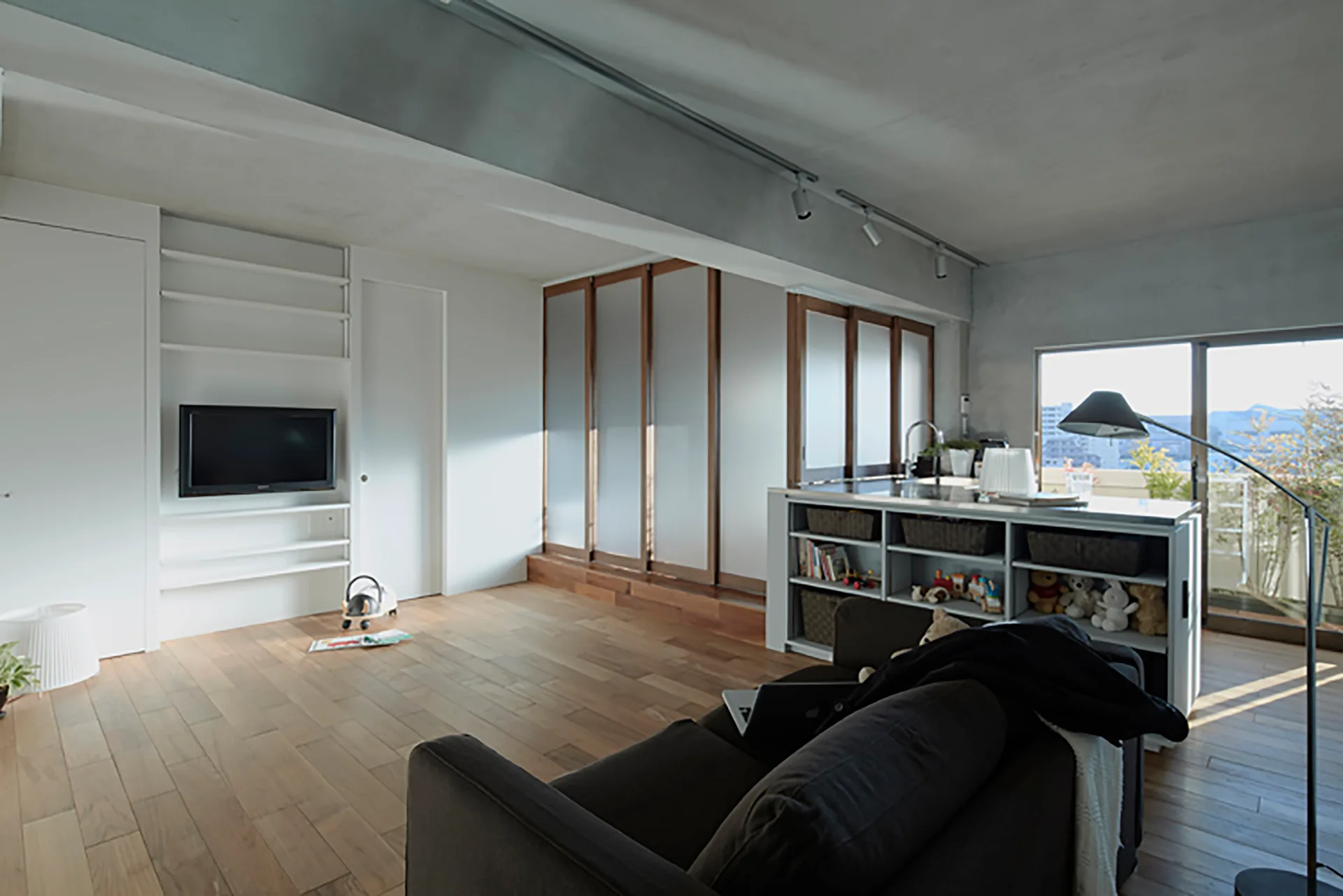 A modern open-plan living room featuring a dark sofa, light wood flooring, and frosted glass sliding partition doors.