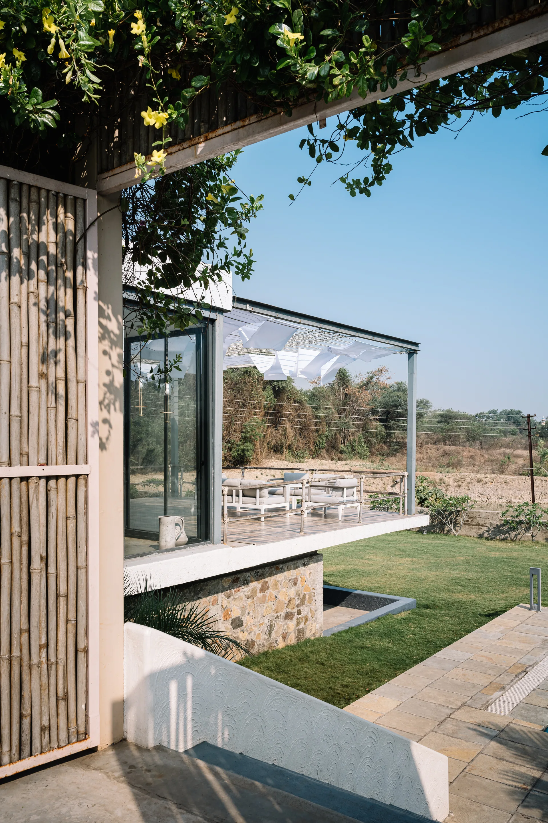 An elevated concrete terrace features a modern seating area shaded by draped white fabric under a metal frame next to a vertical bamboo screen.