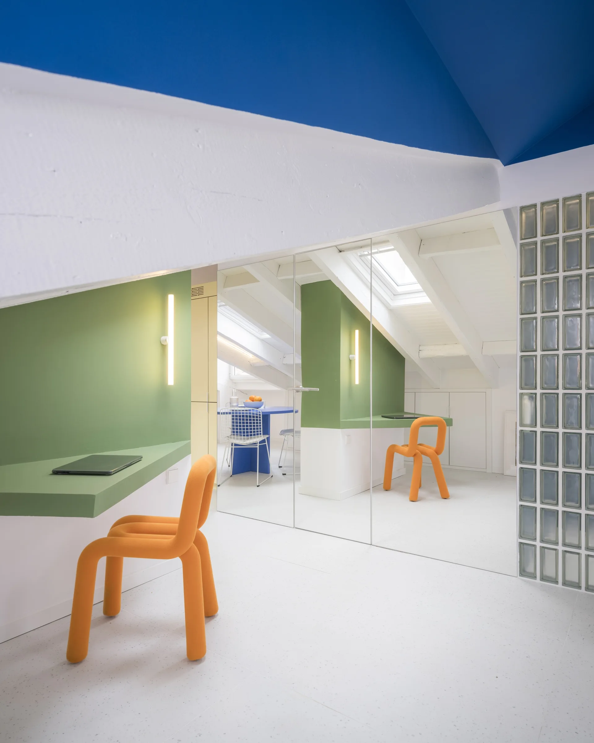 A modern attic home office featuring a floating green desk, a sculptural orange chair, a mirrored wall, and a blue ceiling.