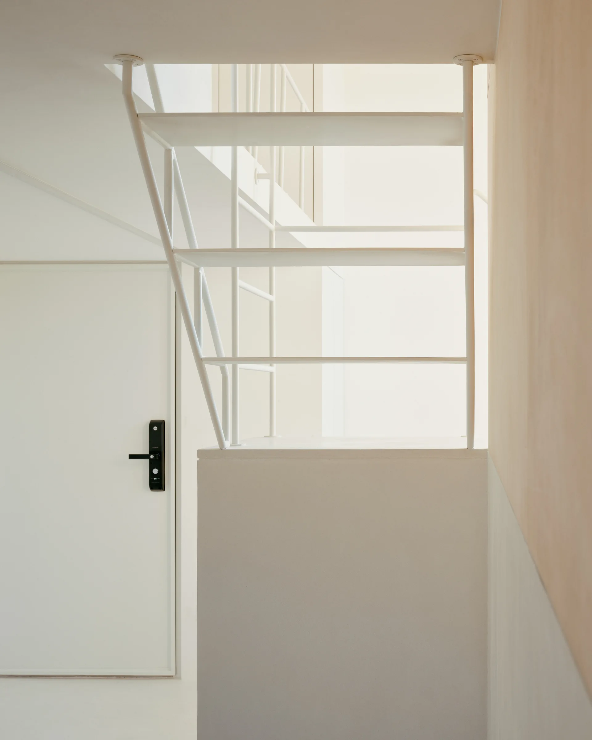 A minimalist white staircase with open metal risers mounted near a white door with a black digital lock.
