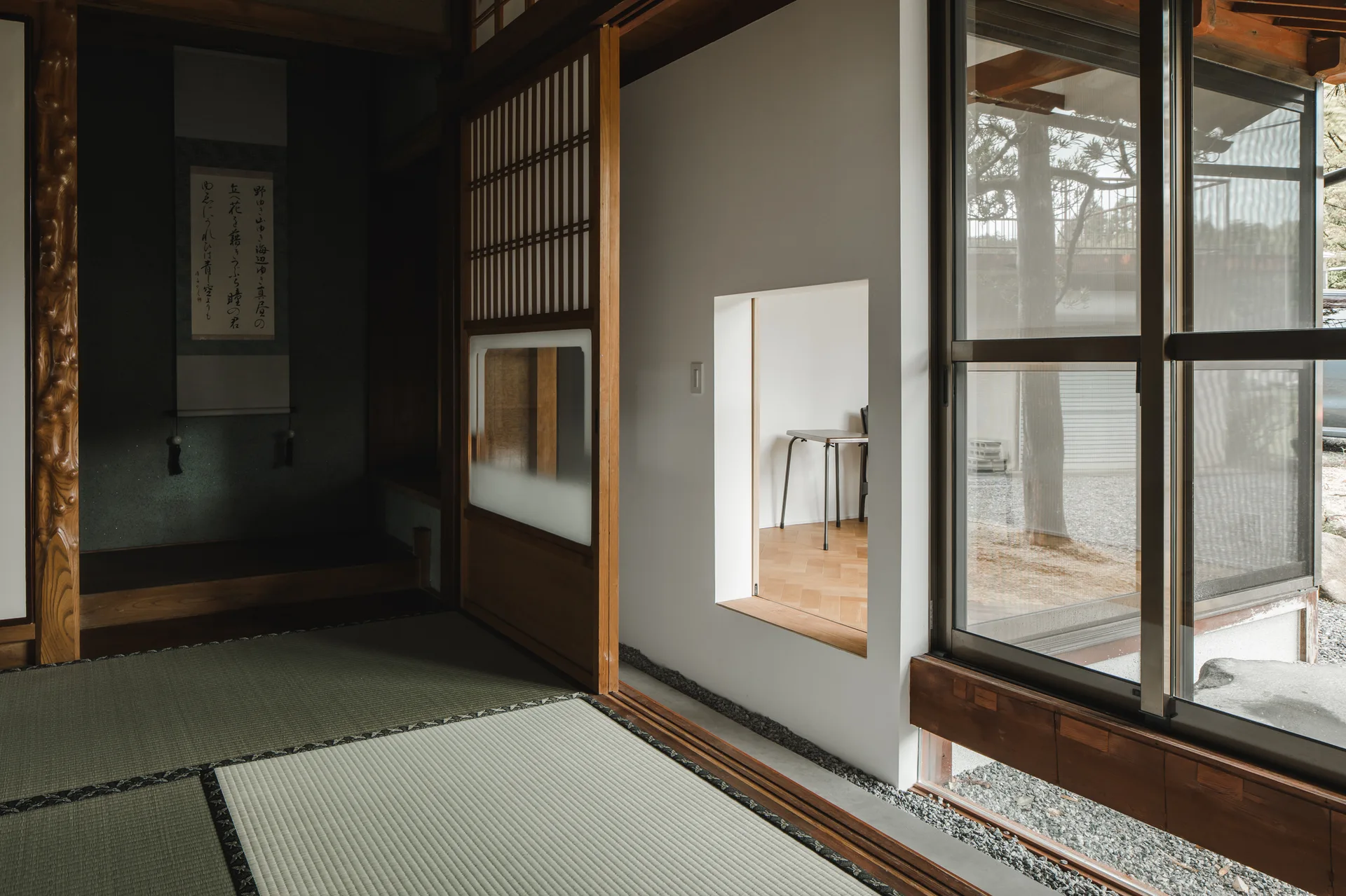 A Japanese interior features tatami mat flooring, a recessed tokonoma alcove, a sliding door, and a square wall cutout looking into another room.